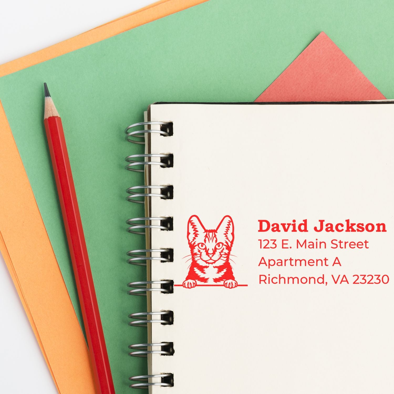 Wood Handle American Shorthair Cat Address Stamp on a notebook, featuring a red cat design with address details. A red pencil and colorful paper are placed beside the notebook.
