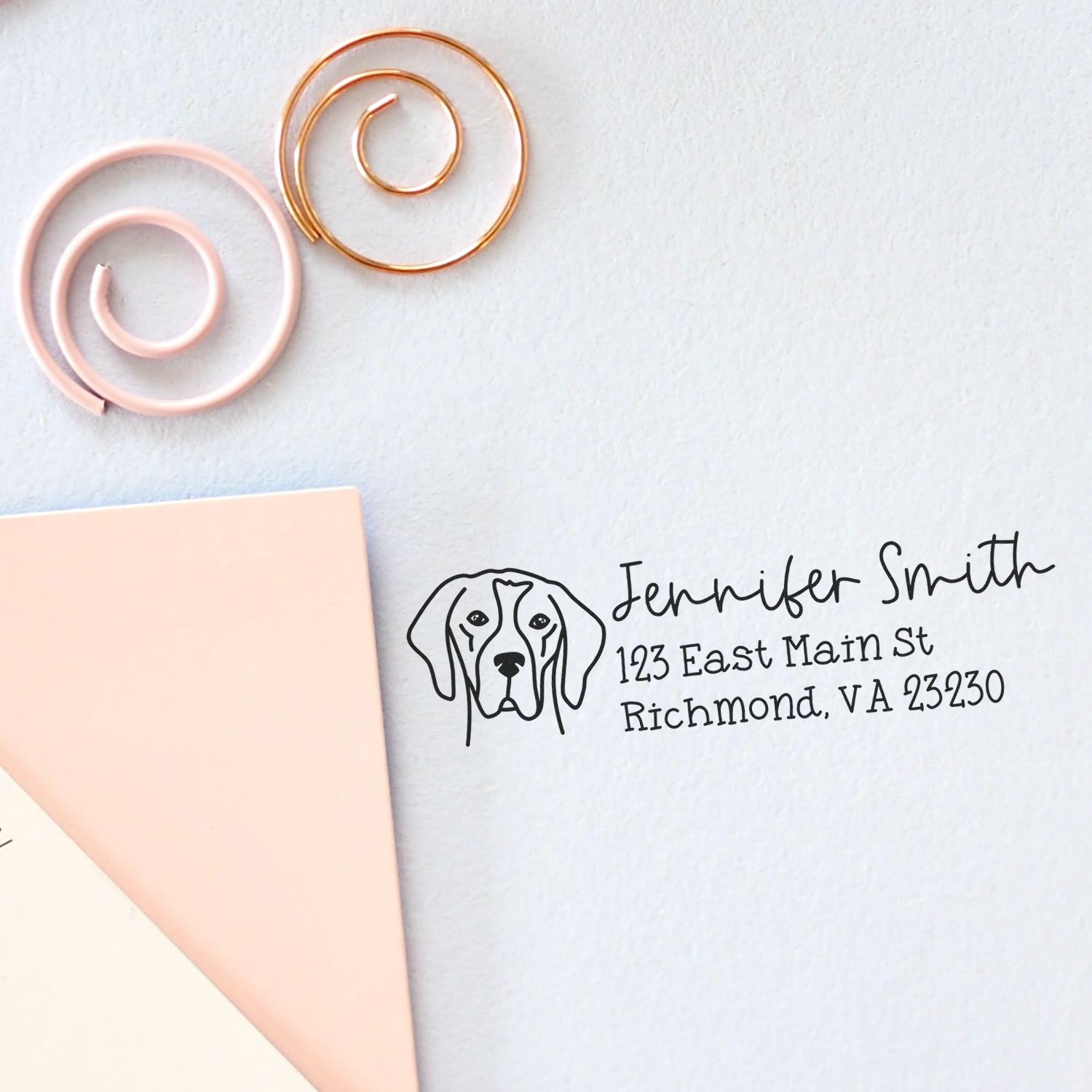 Pastel pink and gold spiral seal samples with a custom address stamp featuring a dog logo and black text on white paper.