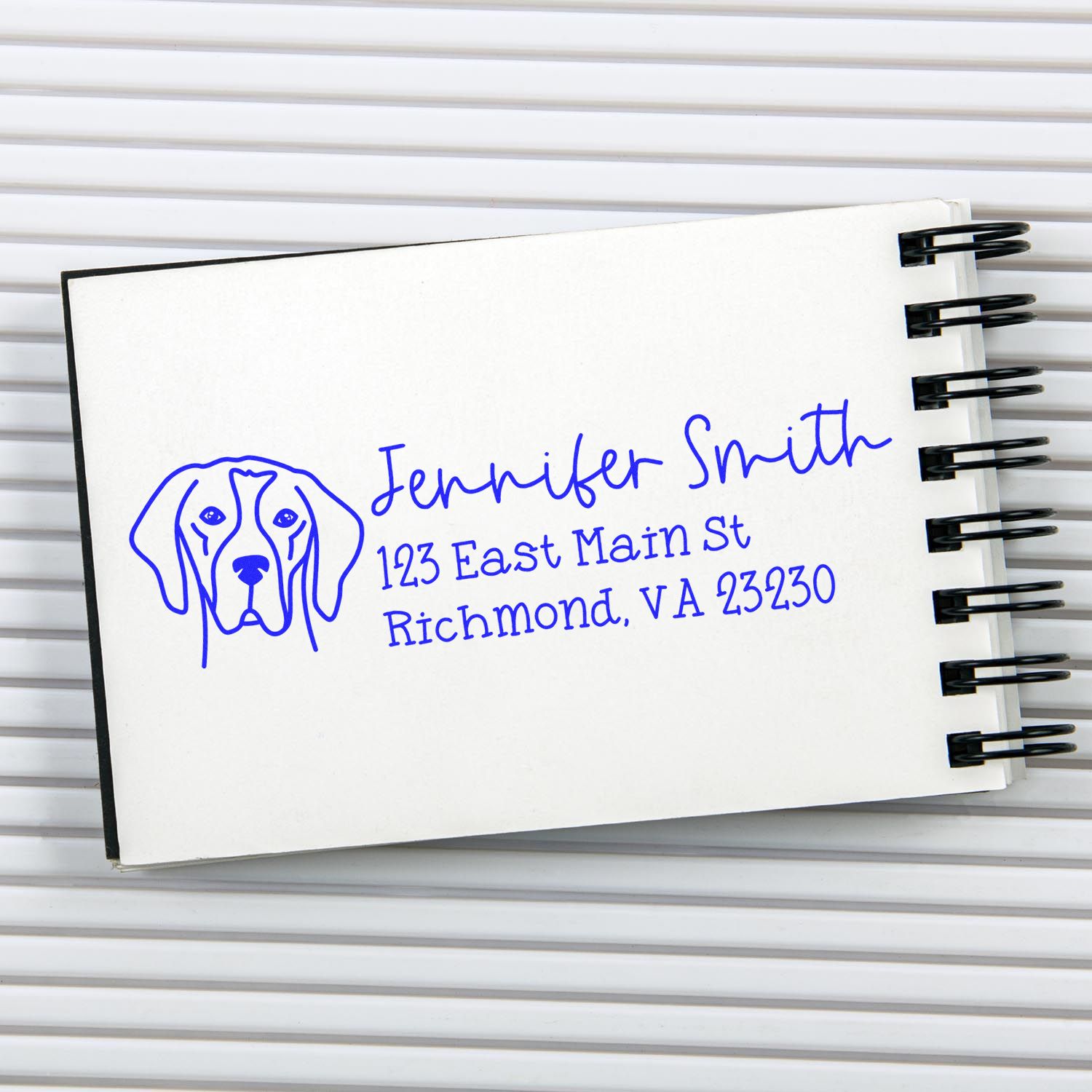 Blue custom address stamp with dog logo, Jennifer Smith, Richmond, VA on white spiral-bound notebook.
