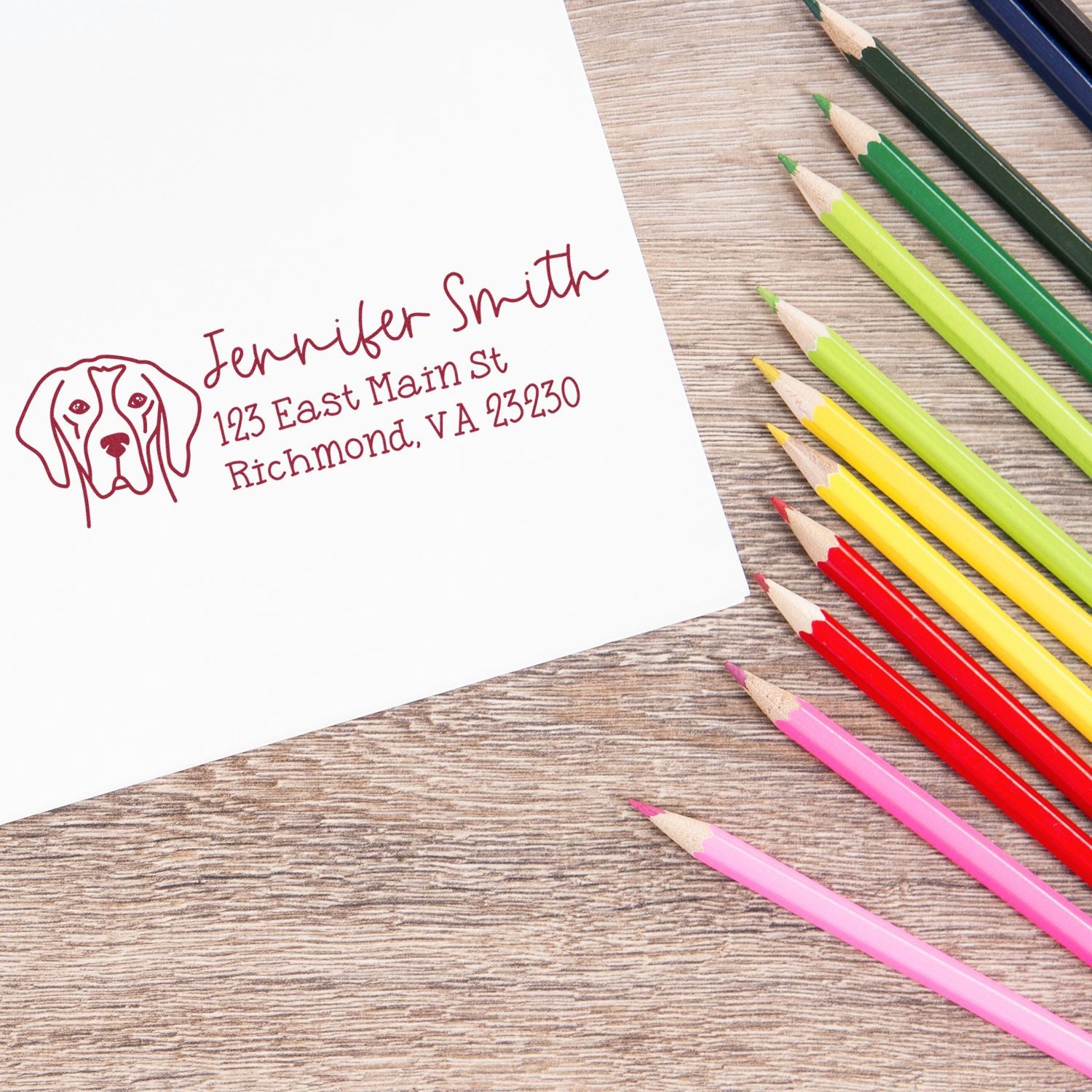 Custom red dog logo stamp and seal on white paper, with colorful pencils on a wood desk