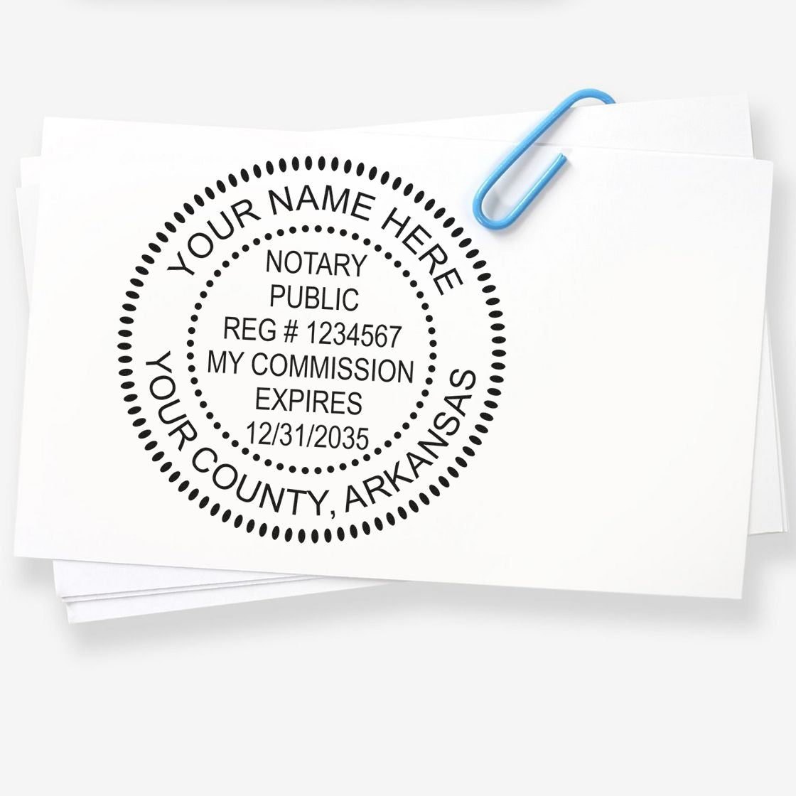 Black custom notary public stamp seal on white papers, clipped with a blue paperclip and circular Arkansas commission text.