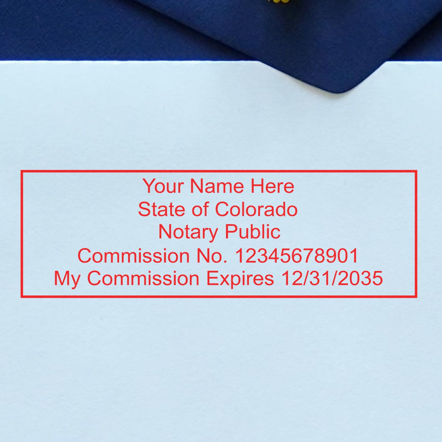 Red Colorado notary public stamp with commission number and expiration date on light blue paper, beneath a dark blue envelope.