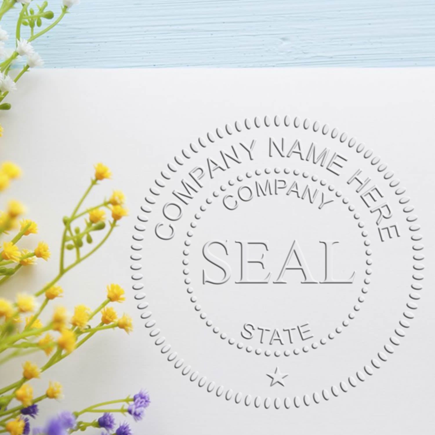 Embossed white circular company seal stamp on white card, with yellow and purple flowers and pale blue background.