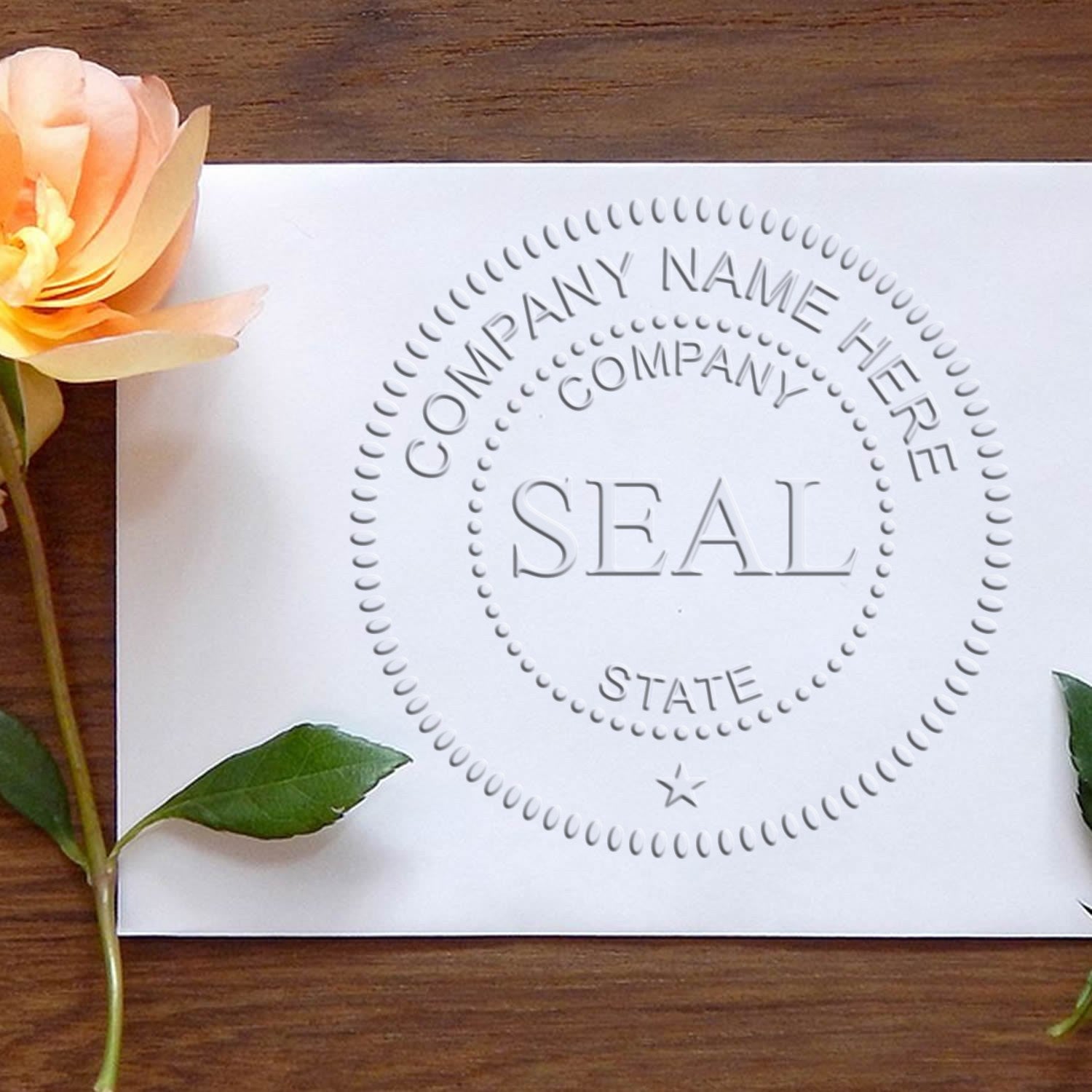 White embossing stamp and seal sample with circular company name and seal design, beside a peach rose on wood.