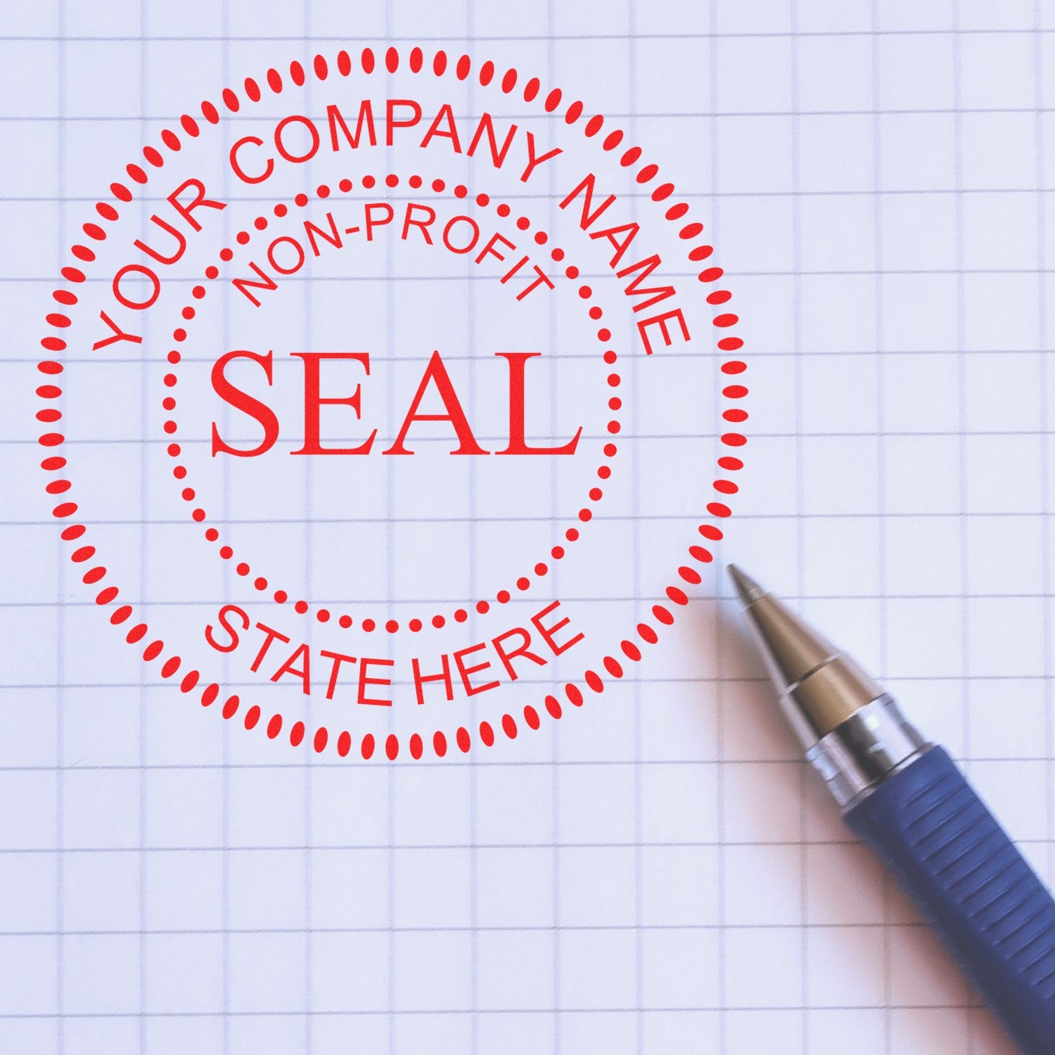 Red circular stamp seal for a non-profit, with customizable company name and state line, on graph paper beside a blue pen.