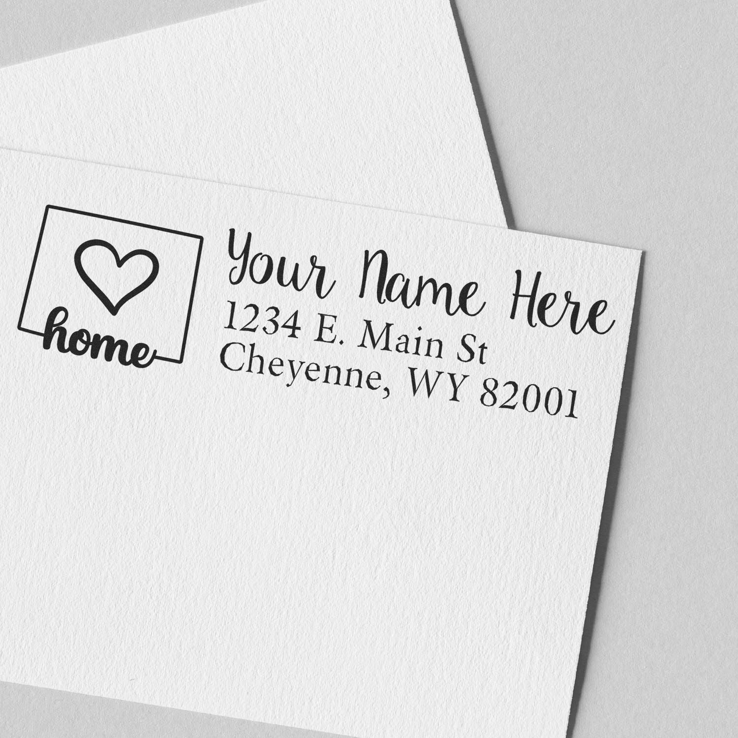 Wood Handle Wyoming Custom Address Rubber Stamp on white paper, featuring a heart and home design with sample address: 1234 E. Main St, Cheyenne, WY 82001.