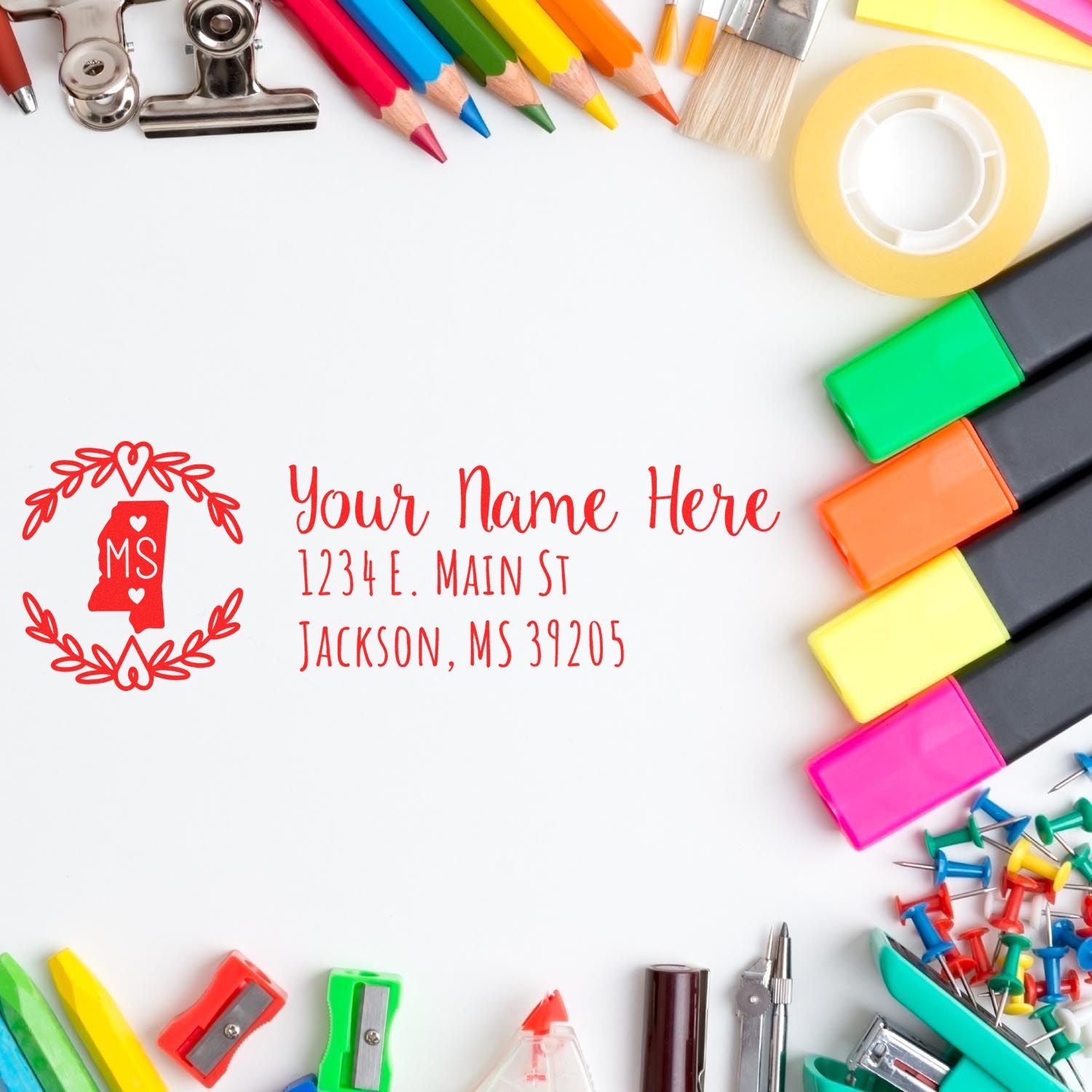 A colorful desk with stationery surrounds a stamped envelope featuring the Mississippi State Custom Return Address Stamp, showcasing a red design with space for a name and address.