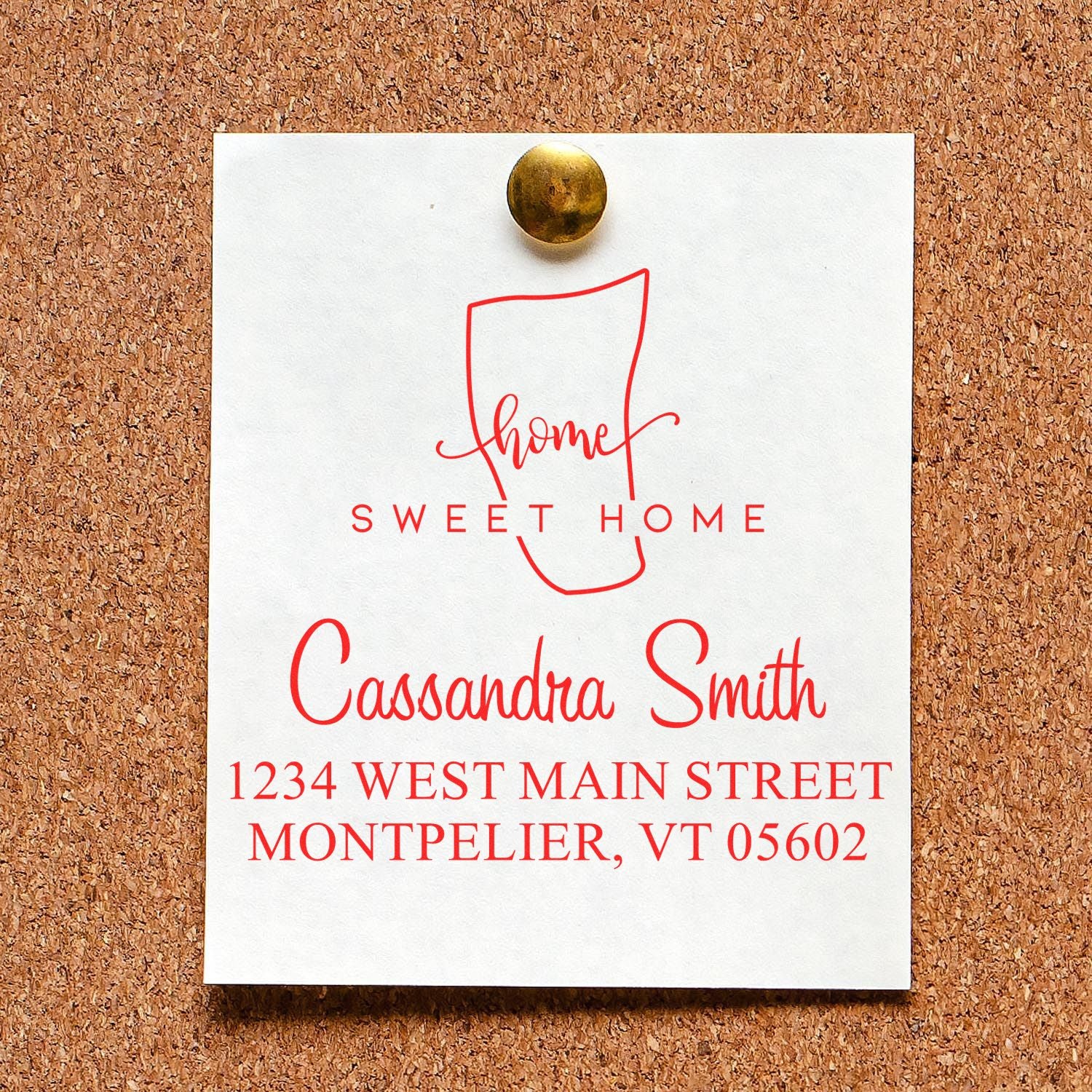 Custom red home address stamp and seal design on white card, pinned with brass tack against a corkboard.