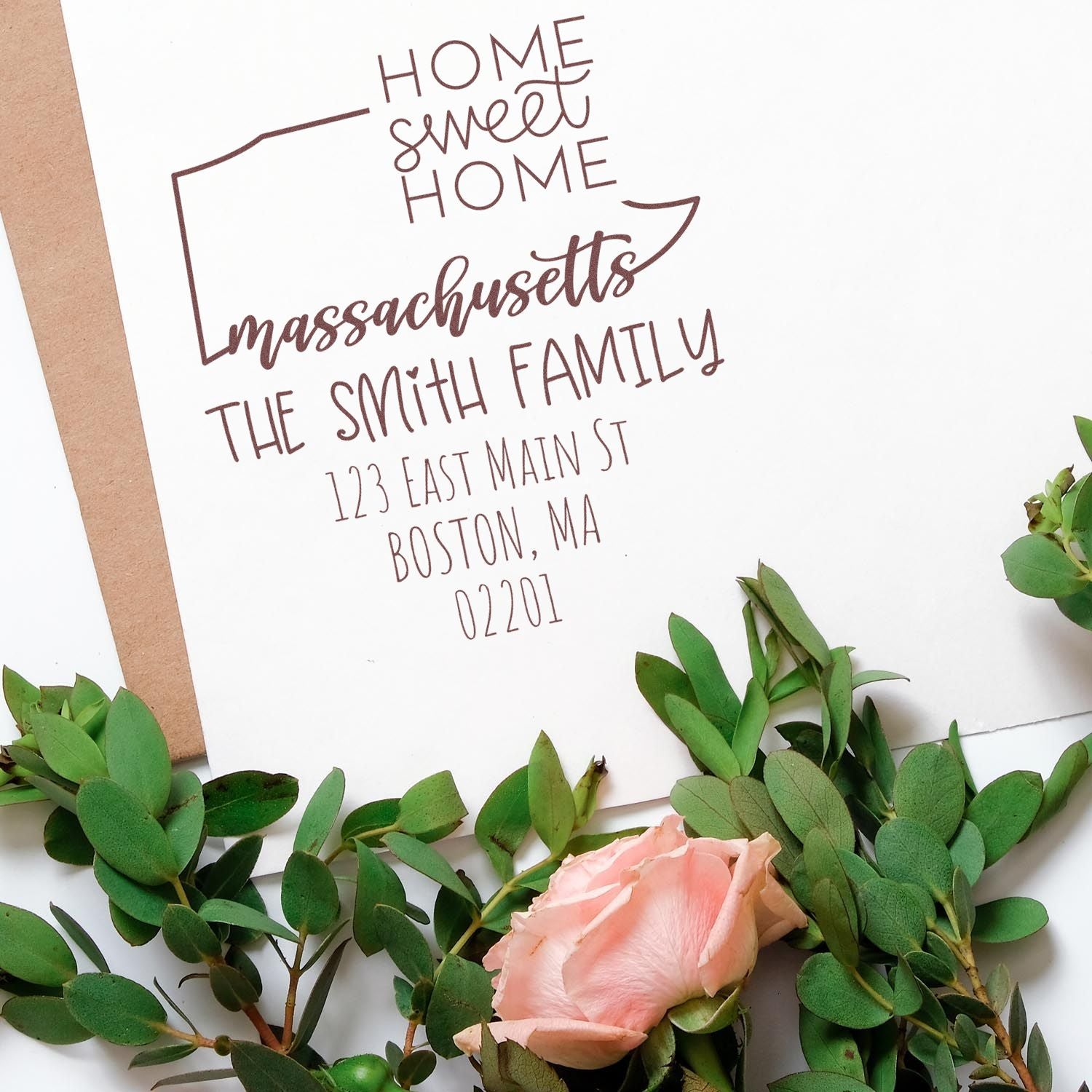 Brown custom home address stamp and seal on white paper, framed by green leaves and a pink rose.