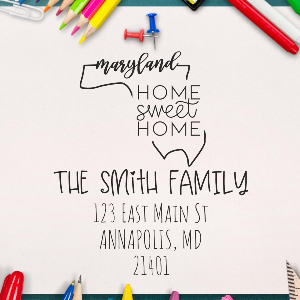 Custom black Maryland home address stamp and seal with family name, Annapolis address, on white paper with colorful pencils.