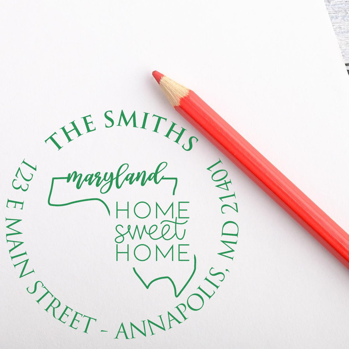 Green custom Maryland home address stamp seal with The Smiths and Home Sweet Home, beside a red pencil on white paper.