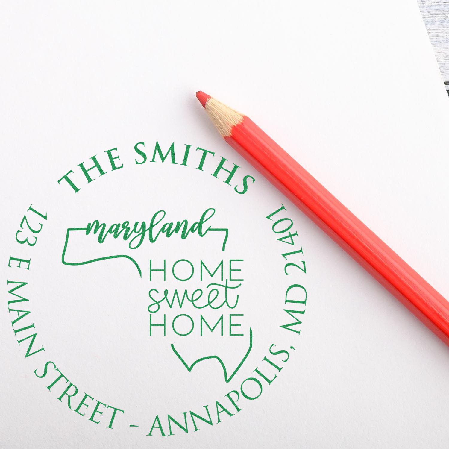 Green custom Maryland home sweet home stamp seal with address text, beside a red pencil on white paper.