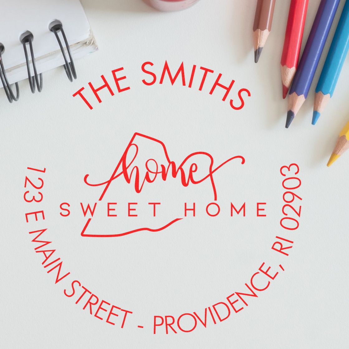 Red custom home stamp seal reading The Smiths and Sweet Home, beside colored pencils on a white background.