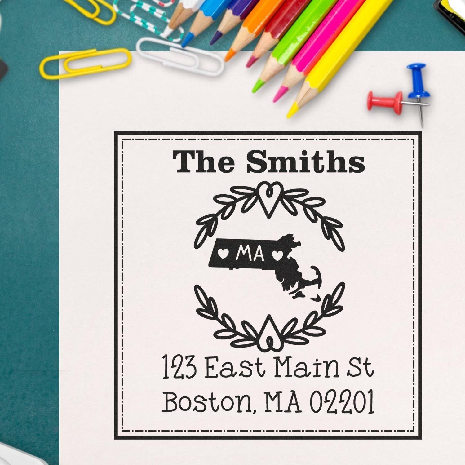 Personalized black address stamp seal for The Smiths, with Massachusetts outline and 123 East Main St on white paper, colorful pencils around
