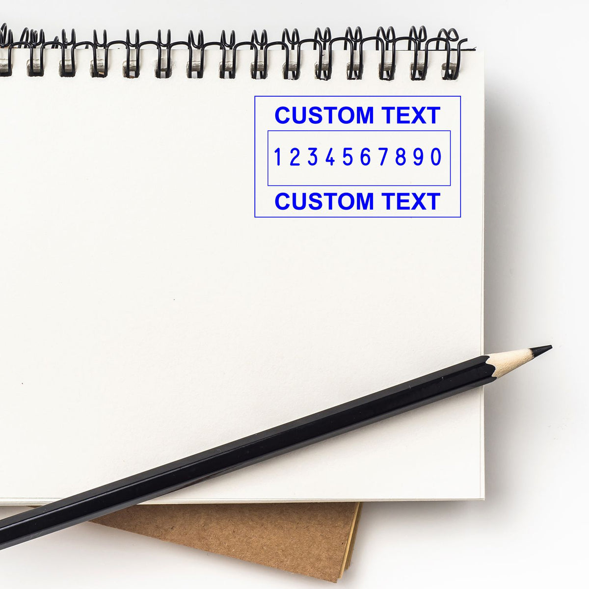 White spiral notebook with blue custom text stamp seal design, 1234567890, and black pencil.