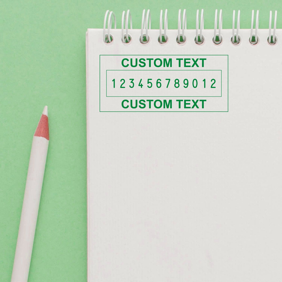 Green custom rubber stamp and seal on white spiral notebook, with bold text and numbers, beside a pink pencil on mint background.
