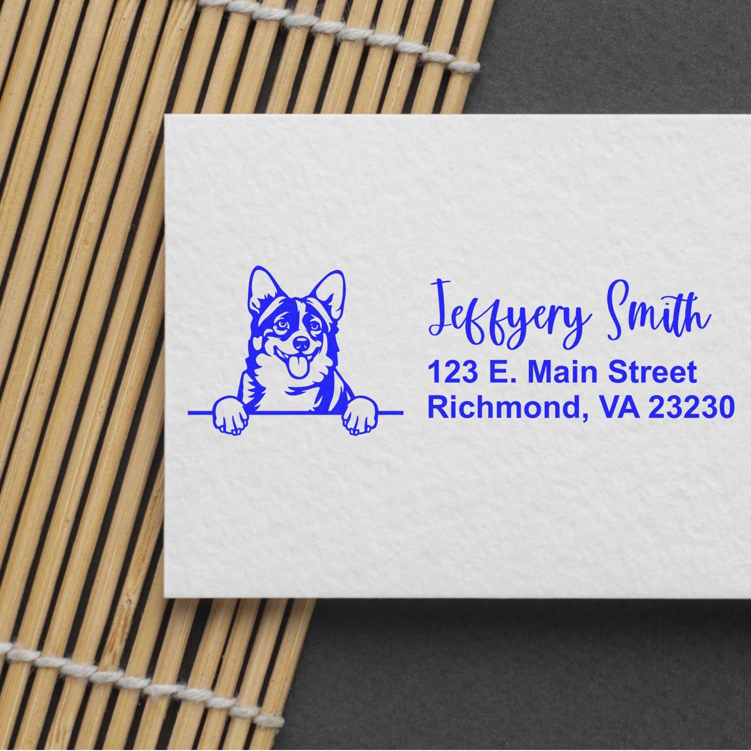 Blue custom stamp with dog logo and Jeffyery Smith address on white paper, beside a bamboo mat.