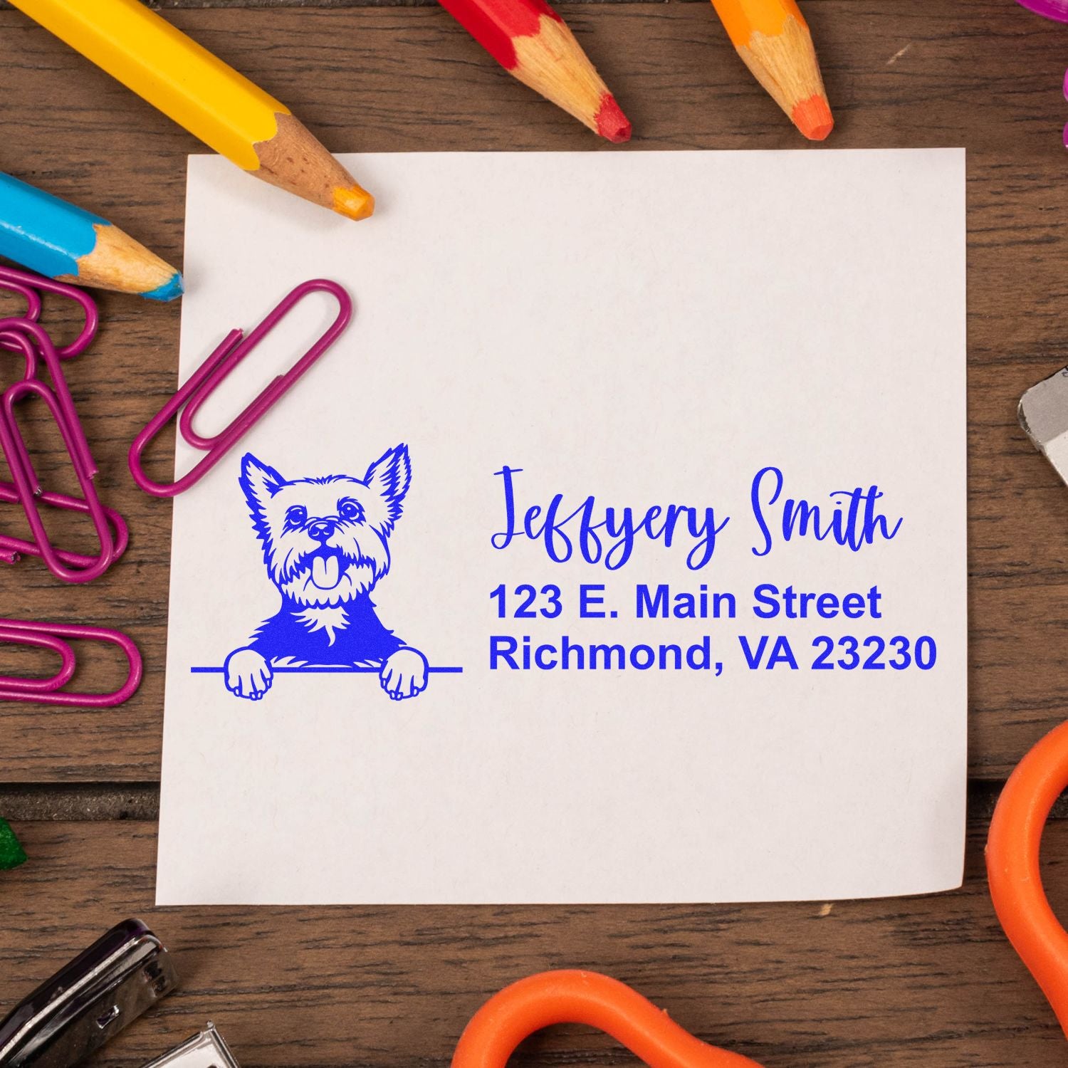Blue custom address stamp with dog illustration for Jeffery Smith on white card, surrounded by colorful pencils and paper clips.