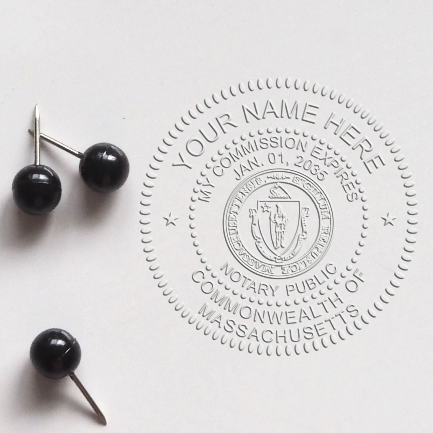 Black metal pins beside an embossed gray notary public seal on white paper, with circular Massachusetts commission details.