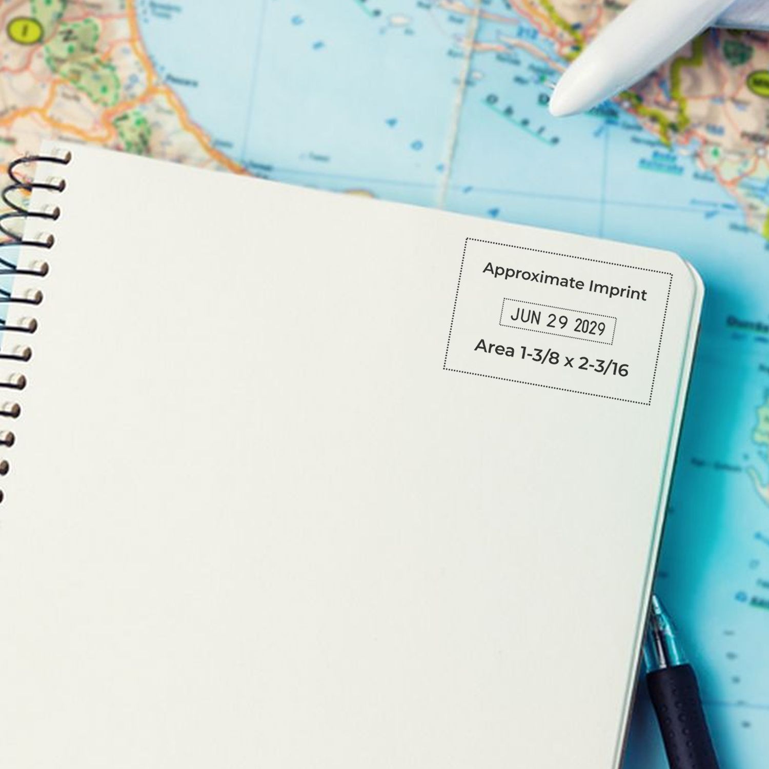Blank spiral notebook with dotted imprint stamp seal, date and size text, over a colorful map with a white pen