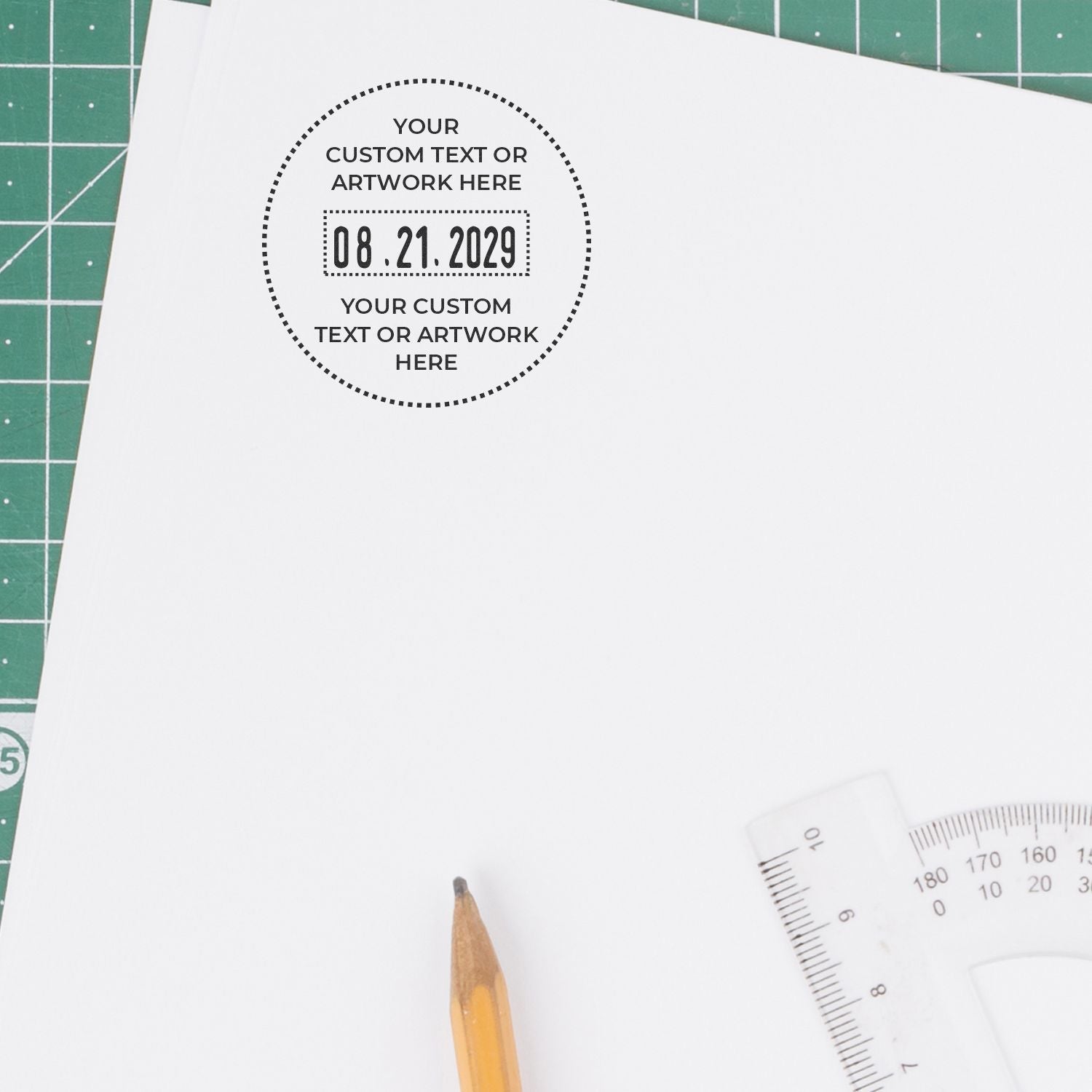 Custom stamp seal on white paper with black dotted circle, text, and 08.21.2029, on a green cutting mat with pencil.