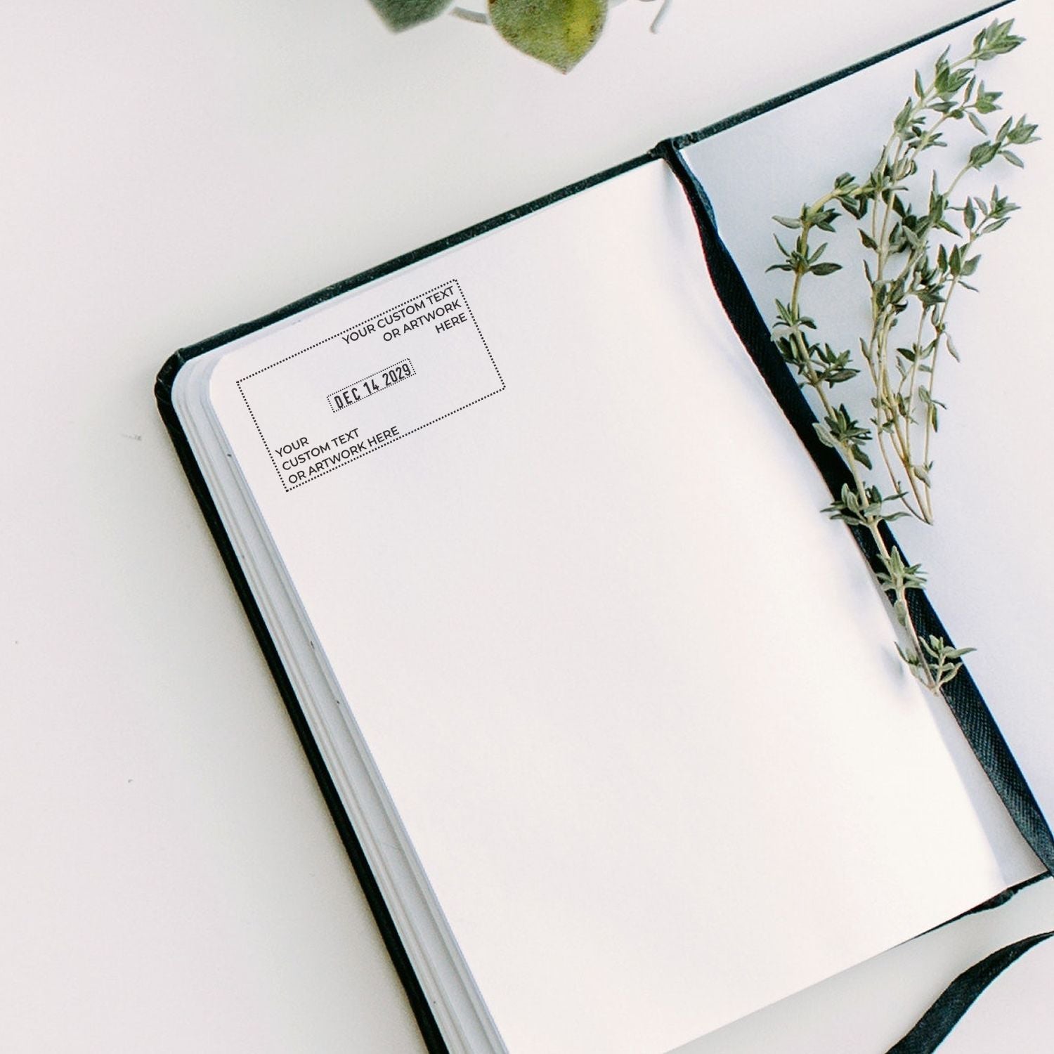 Open white notebook with black ribbon, custom stamp and seal area, and green botanical sprig design.