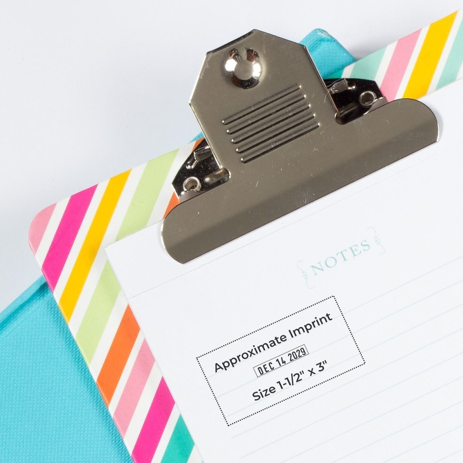 Silver metal stamp seal over striped pastel notes pad and turquoise folder, showing approximate imprint label.