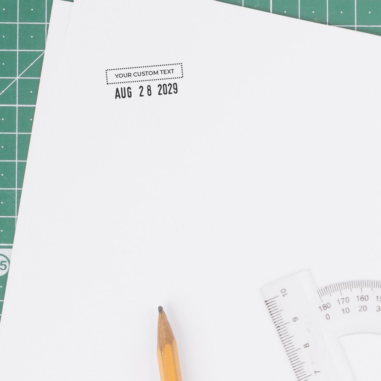 Custom stamp and seal date impression in black on white paper, with a green cutting mat, pencil, and clear ruler.