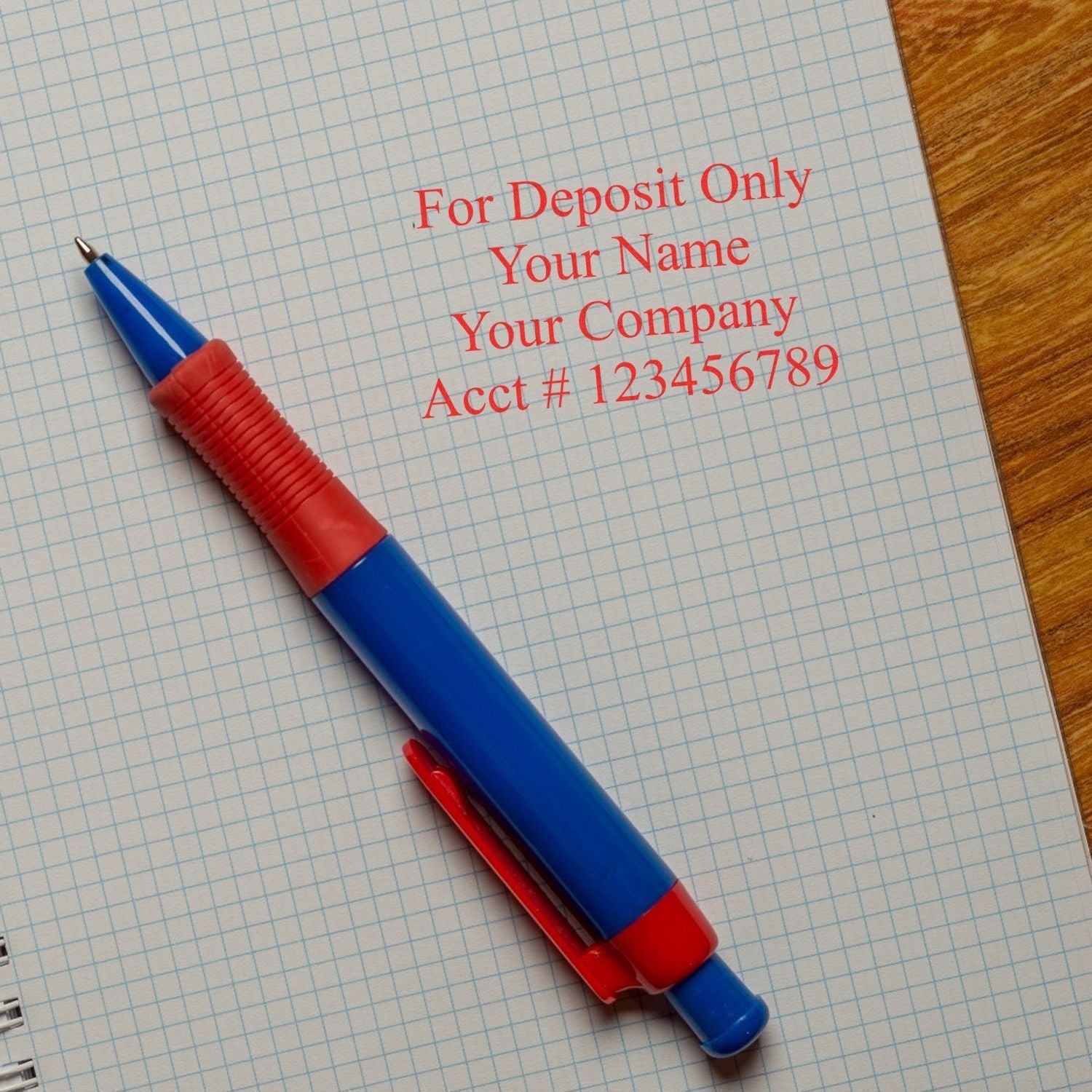 A blue and red pen on graph paper with a stamped message using the 4 Line Regular Rubber Check Endorsement Stamp, reading For Deposit Only Your Name Your Company Acct # 123456789 .