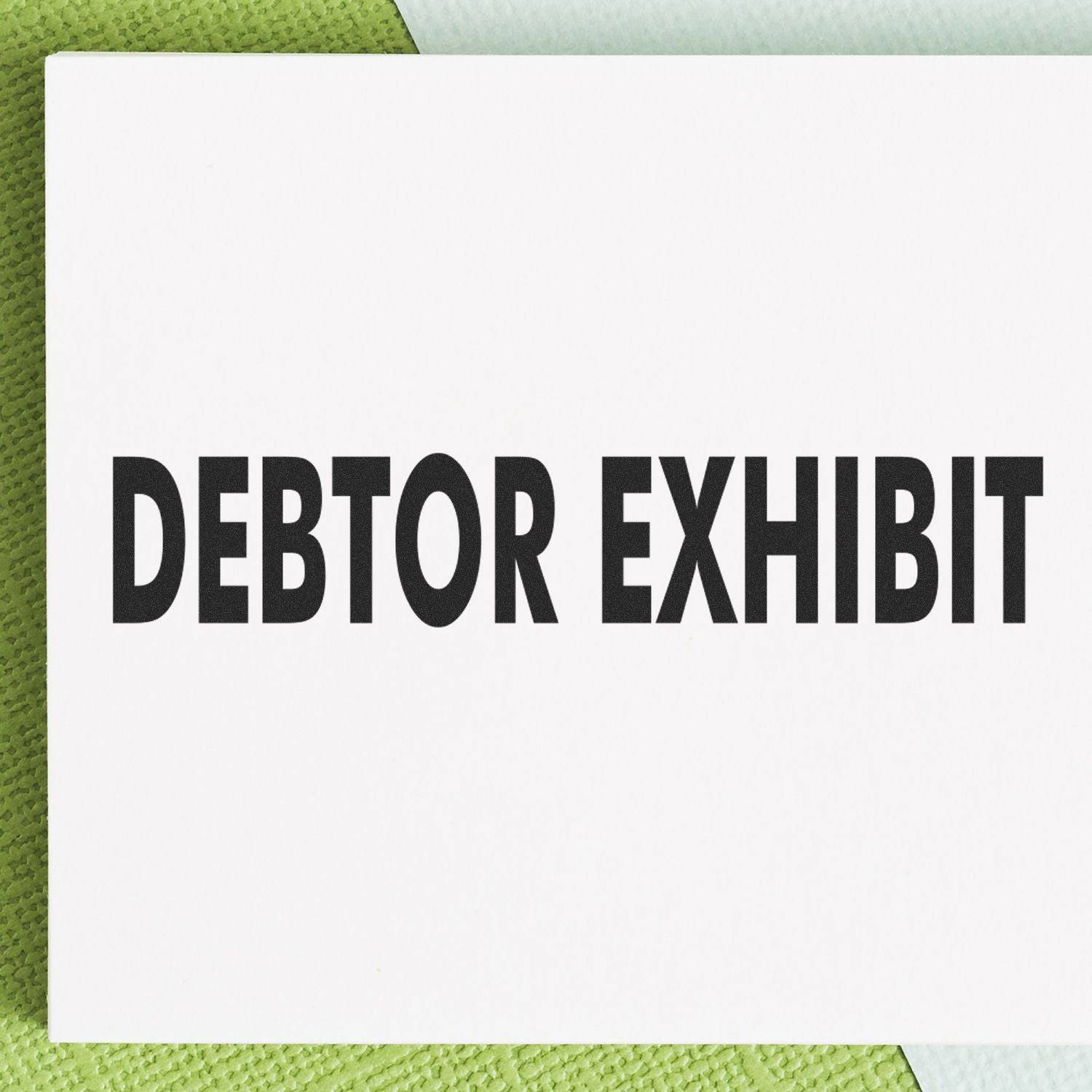 Large Pre-Inked Debtor Exhibit Stamp with bold black text on a white background, placed on a textured green and white surface.