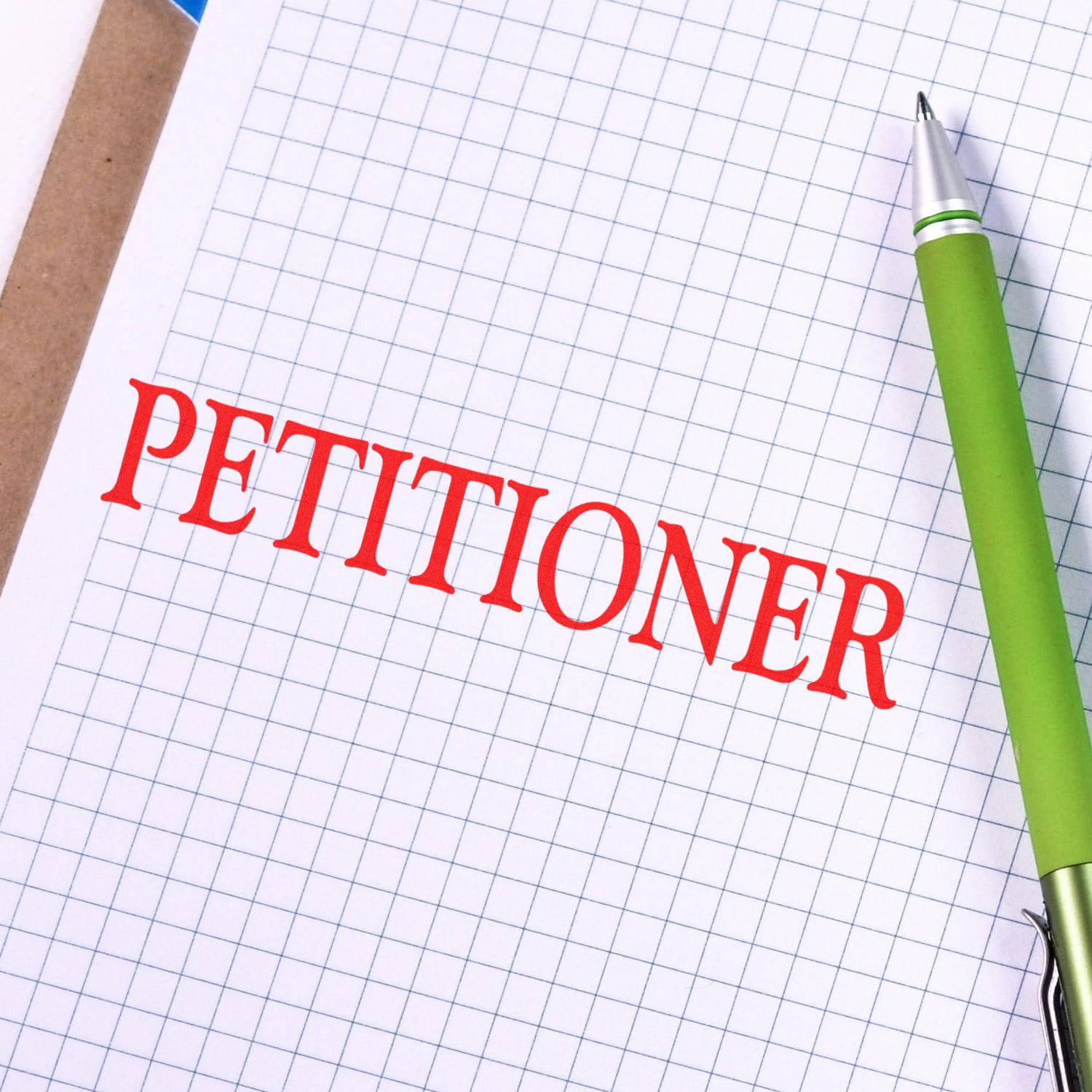Large Pre-Inked Petitioner Stamp in red ink on graph paper with a green pen beside it.