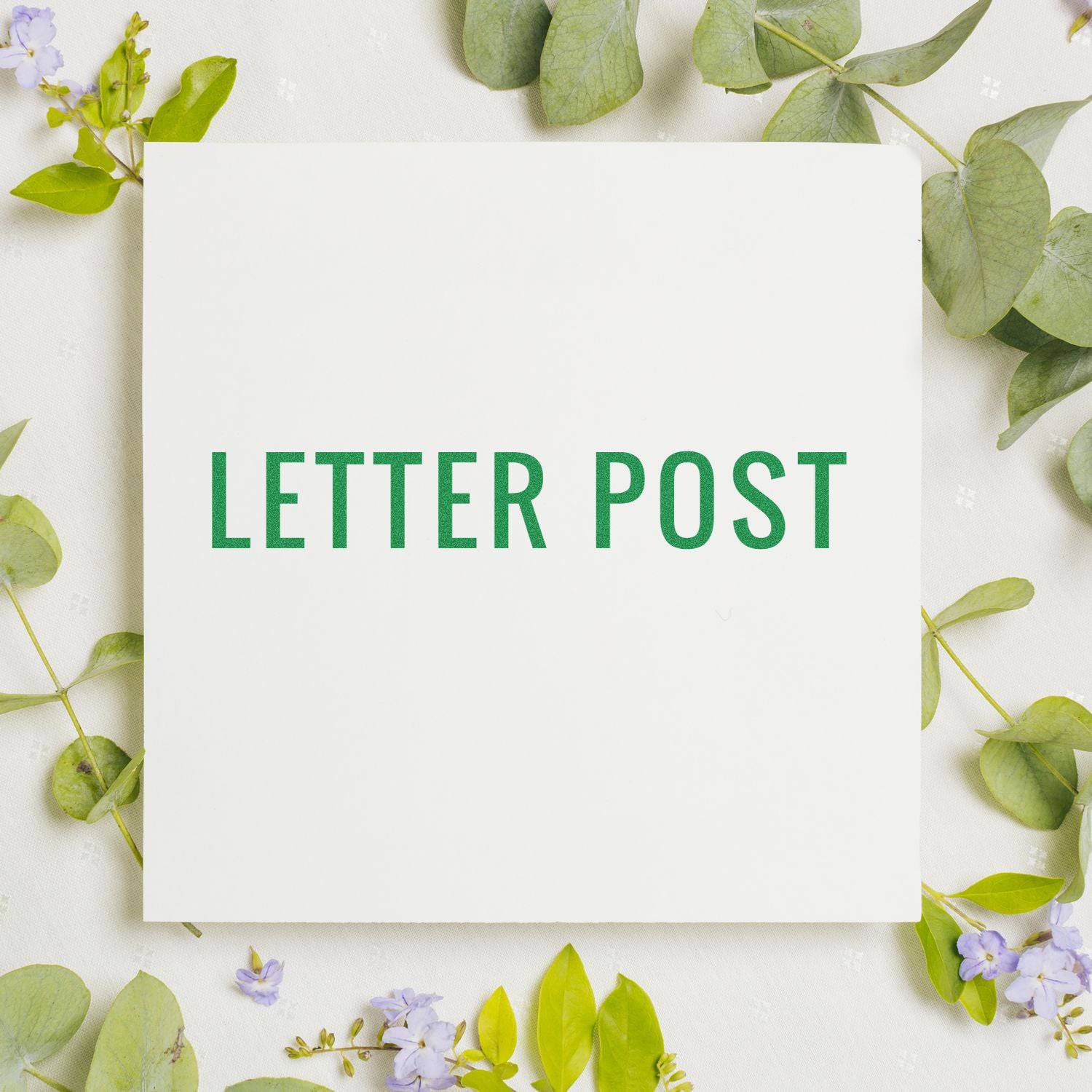 Large Pre-Inked Letter Post Stamp in green ink on white paper, surrounded by green leaves and small purple flowers.