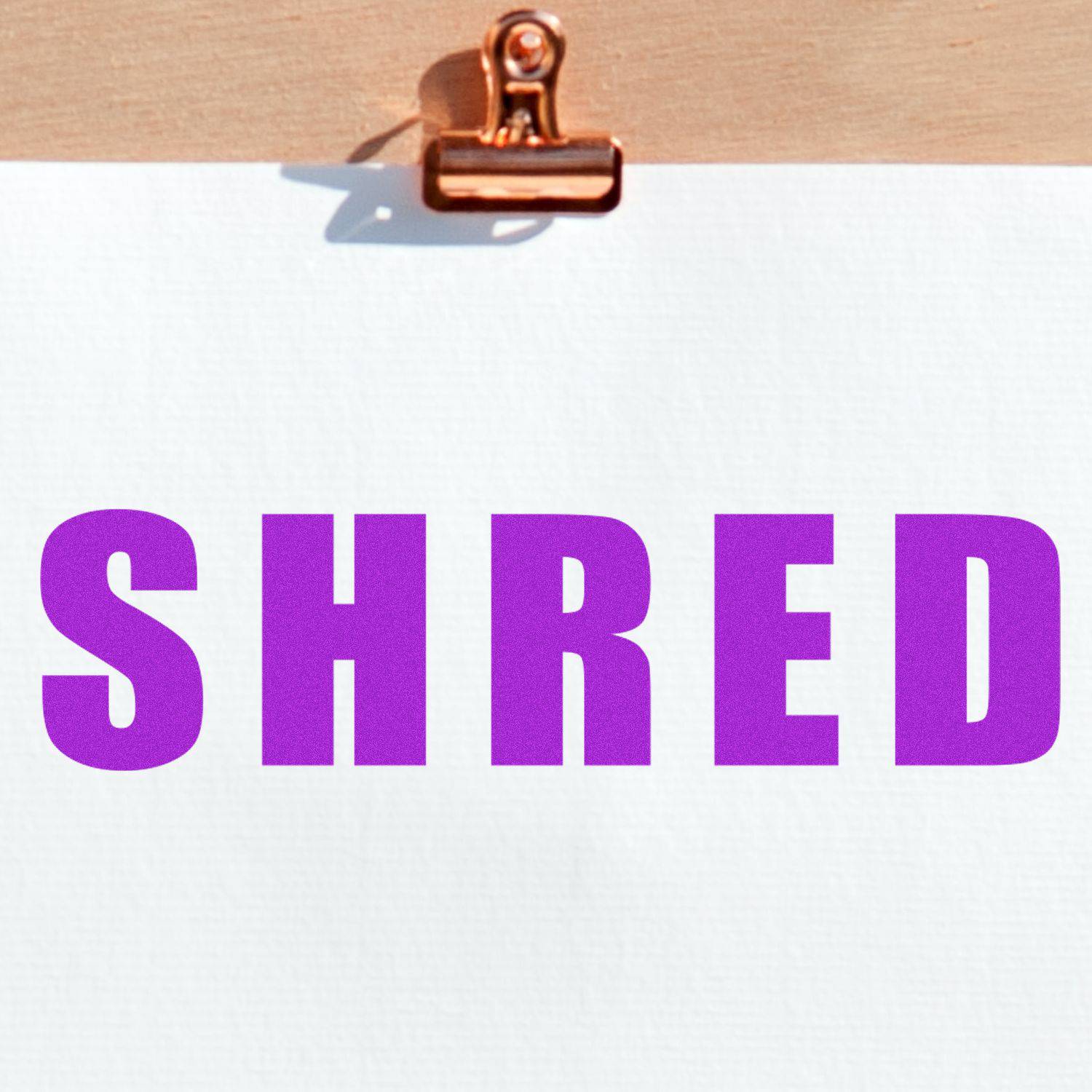 Large Pre-Inked Bold Shred Stamp imprinting the word SHRED in bold purple letters on white paper clipped to a wooden board.
