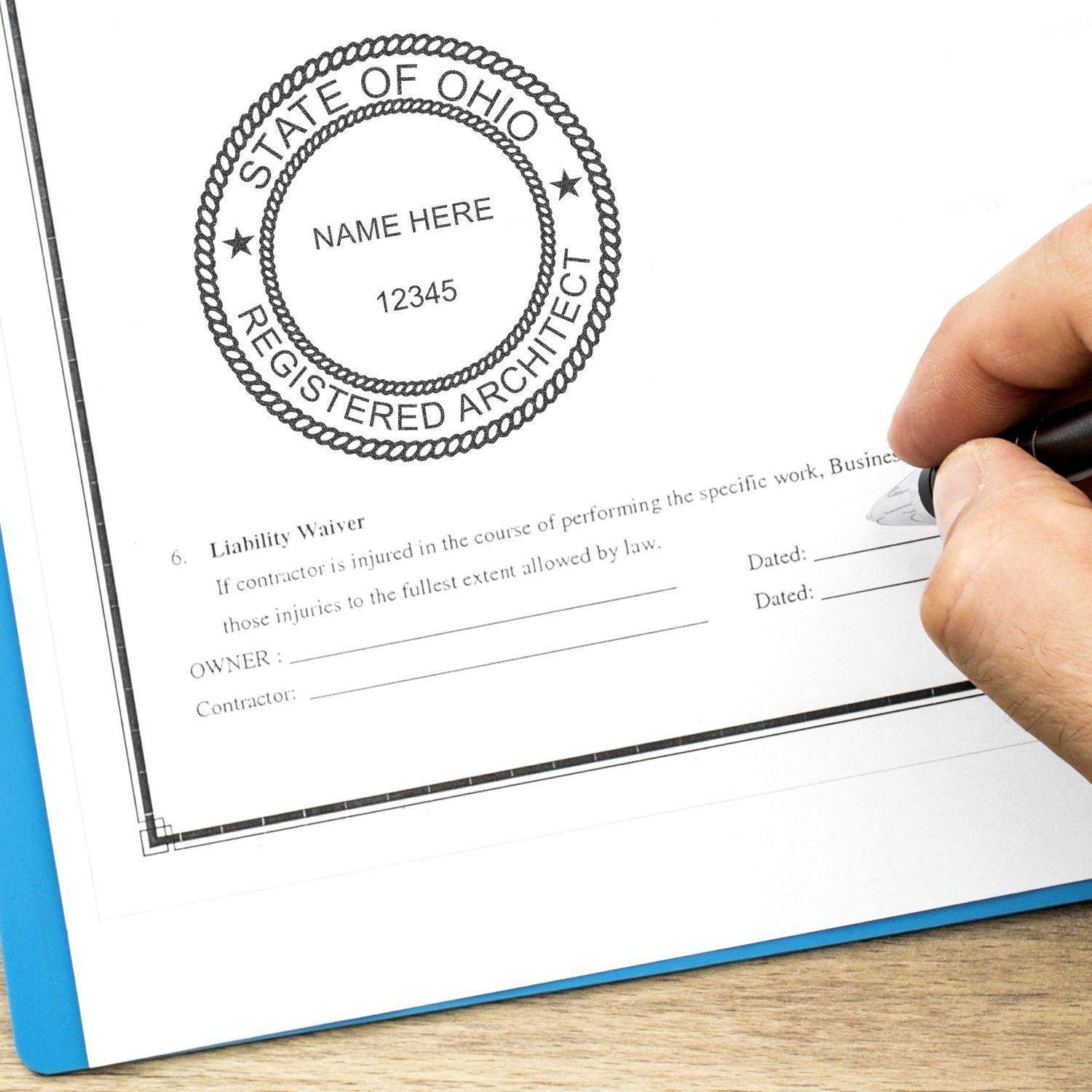 A hand holding a pen next to a document stamped with the Architect Regular Rubber Stamp of Seal, featuring a circular design with State of Ohio Registered Architect and space for a name and number.
