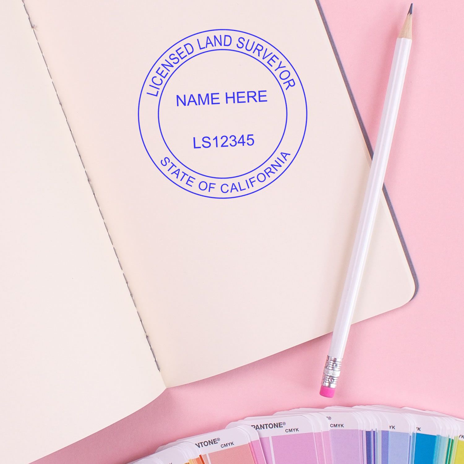 Premium MaxLight Pre-Inked California Surveyors Stamp on an open notebook with a pencil and color swatches on a pink background.