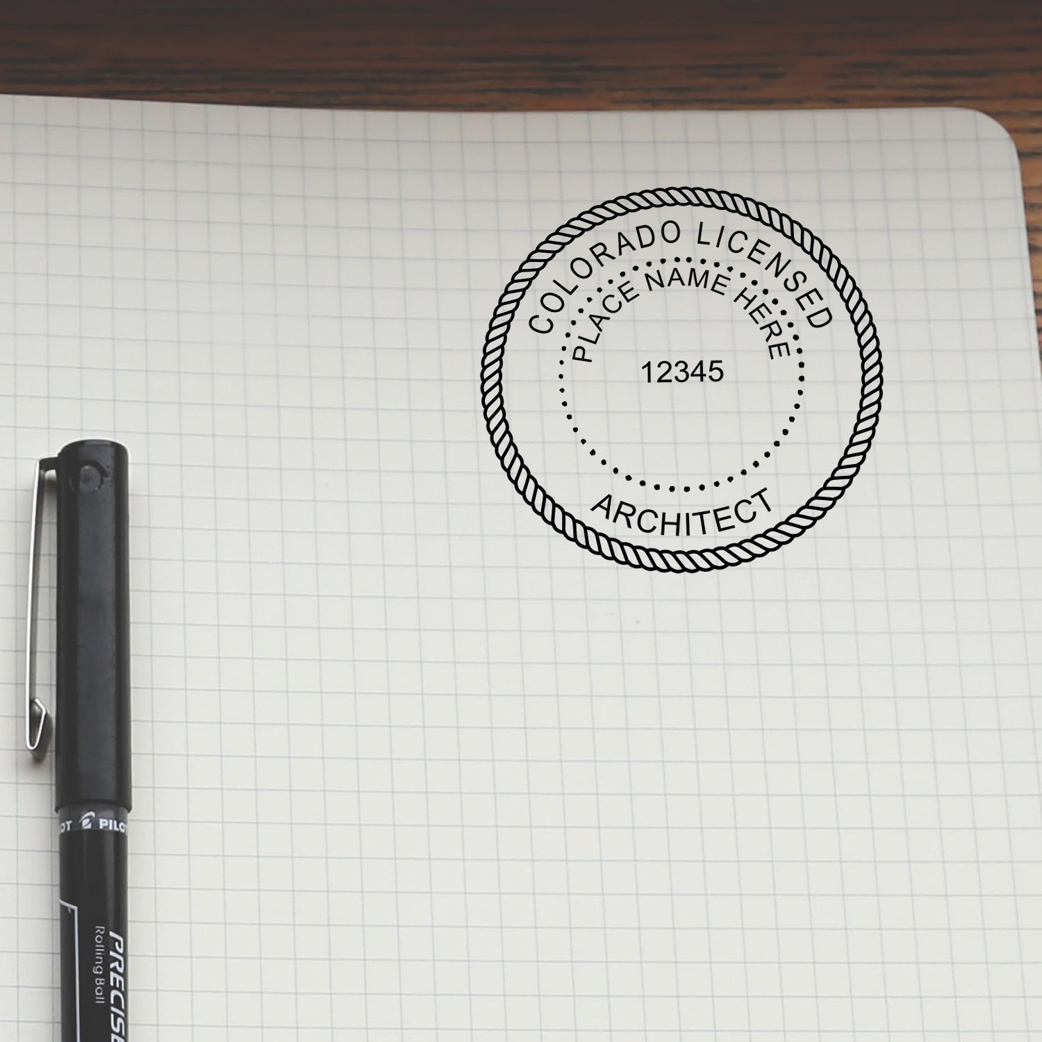 Self Inking Colorado Architect Stamp used on a grid notebook page next to a black pen.