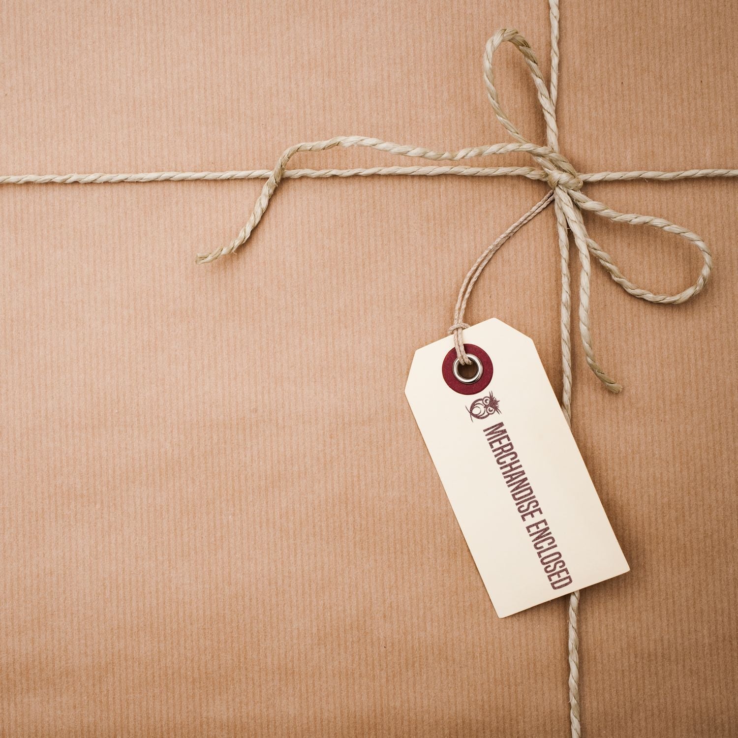 A brown package tied with twine, featuring a tag stamped with MERCHANDISE ENCLOSED using the Slim Stamp 1854 Customized Pre-Inked Stamp 11/16 x 2-1/8.