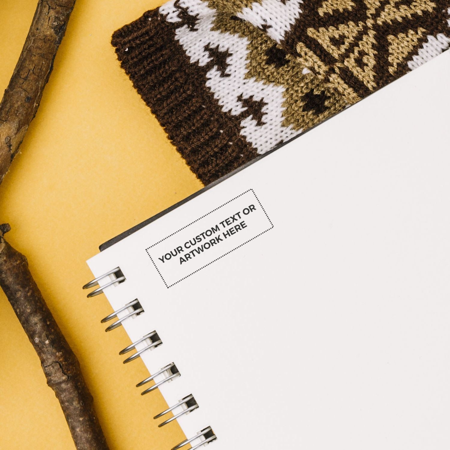 Custom Self Inking Stamp Trodat 4915 Size 1 x 2-3/4 on a spiral notebook with a knitted item and wooden sticks in the background.