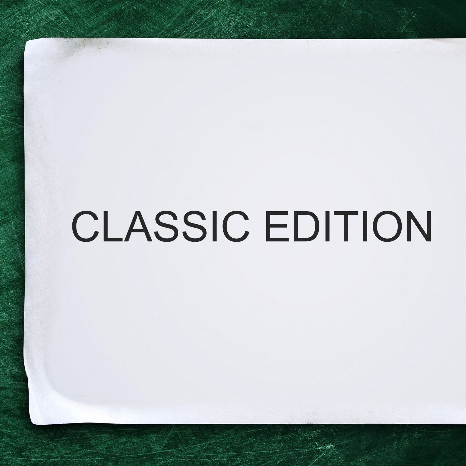 Custom Rubber Stamp Size 2 x 9 used to stamp CLASSIC EDITION on a white paper against a green chalkboard background.