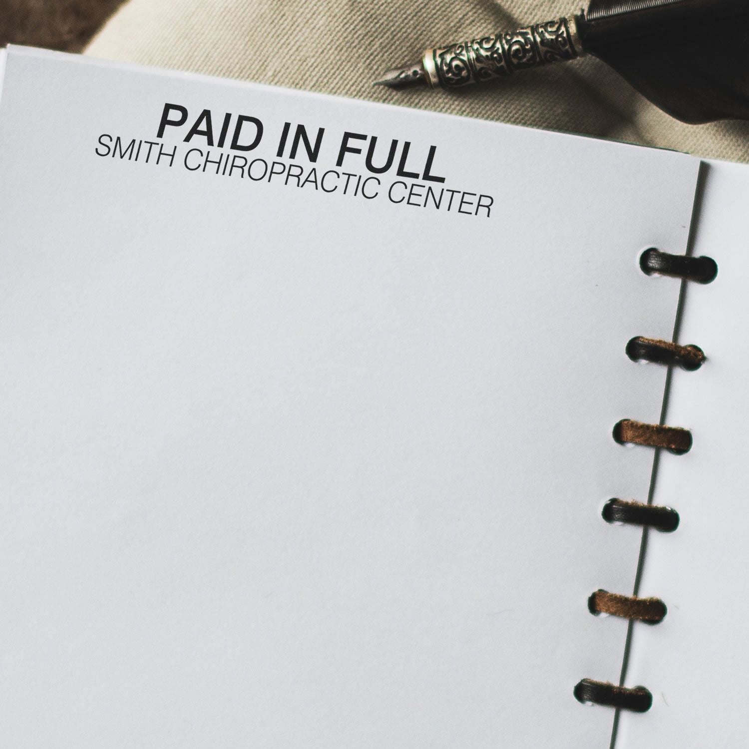 2 Line Custom Rubber Stamp with Wood Handle used to stamp 'PAID IN FULL SMITH CHIROPRACTIC CENTER' on a white paper in a notebook.
