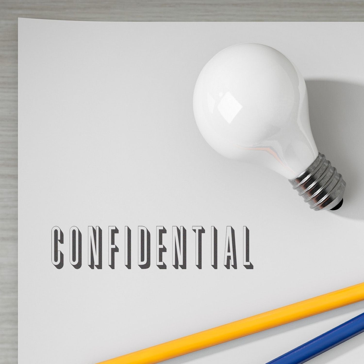 MaxLight XL2-720 Custom Pre-Inked Business Stamp 1 x 4 used to stamp CONFIDENTIAL on paper, with a light bulb and pencils nearby.