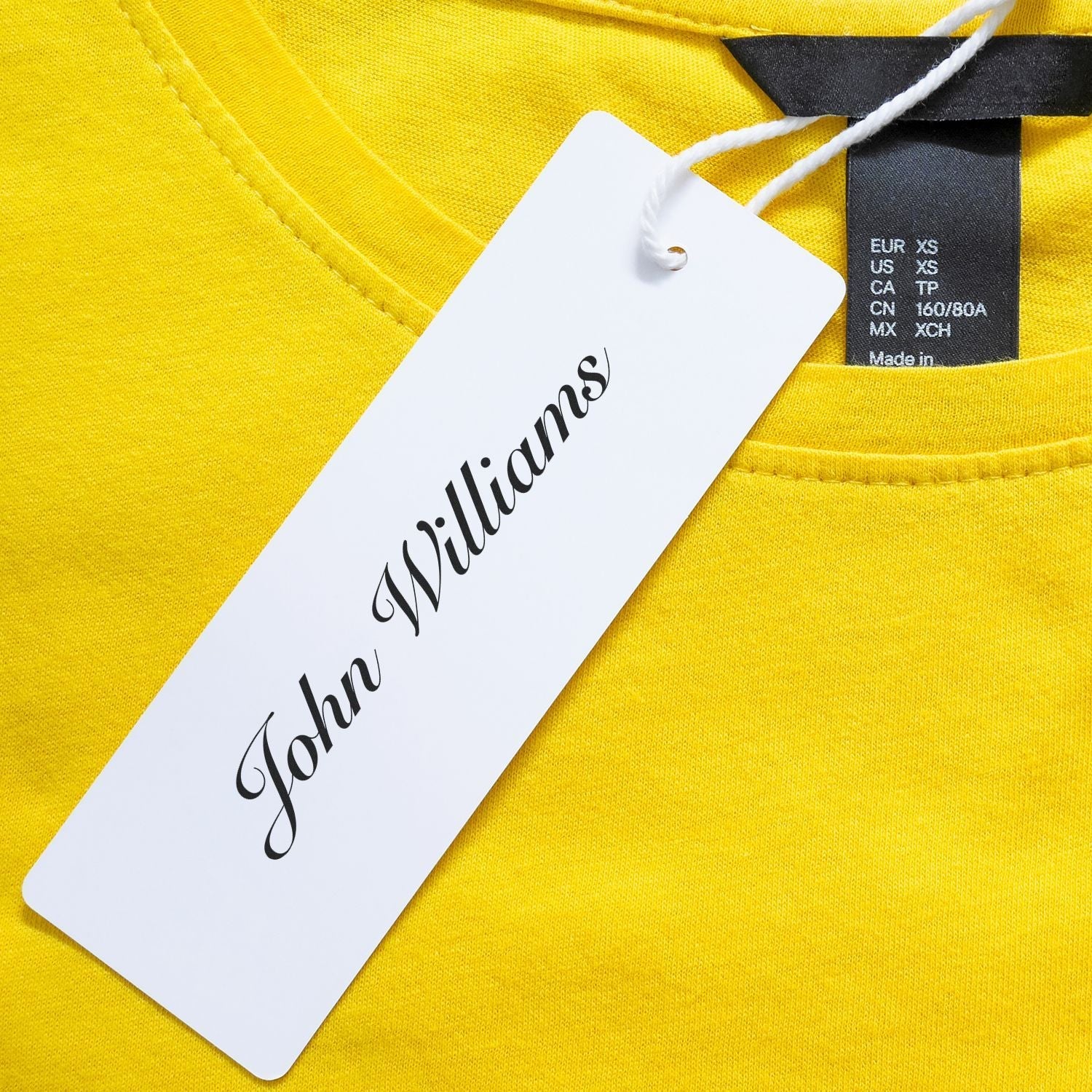 A yellow shirt with a white tag labeled John Williams stamped using the Custom Rubber Stamp Size 1 x 6.
