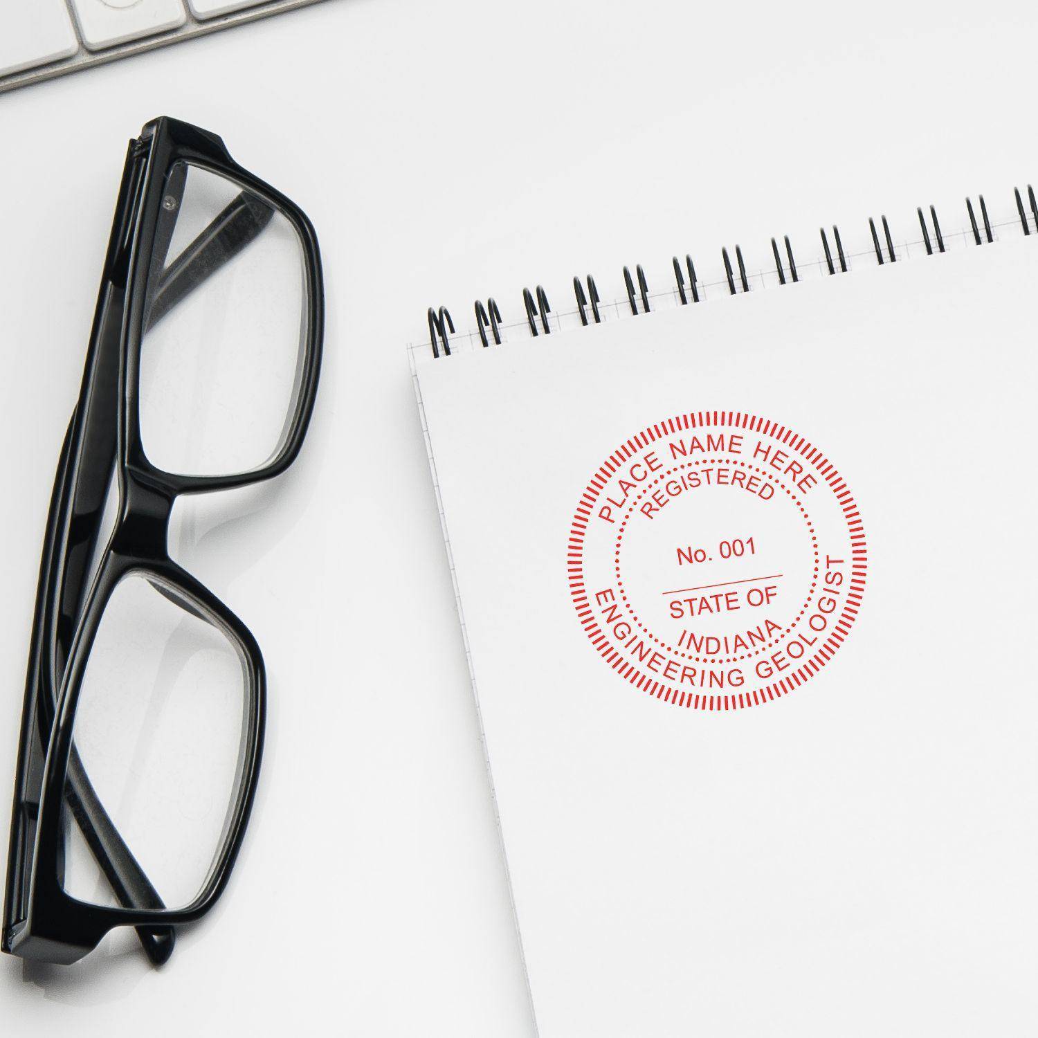 Engineering Geologist Regular Rubber Stamp of Seal in red ink on a white notepad, placed next to a pair of black-framed glasses and a keyboard.
