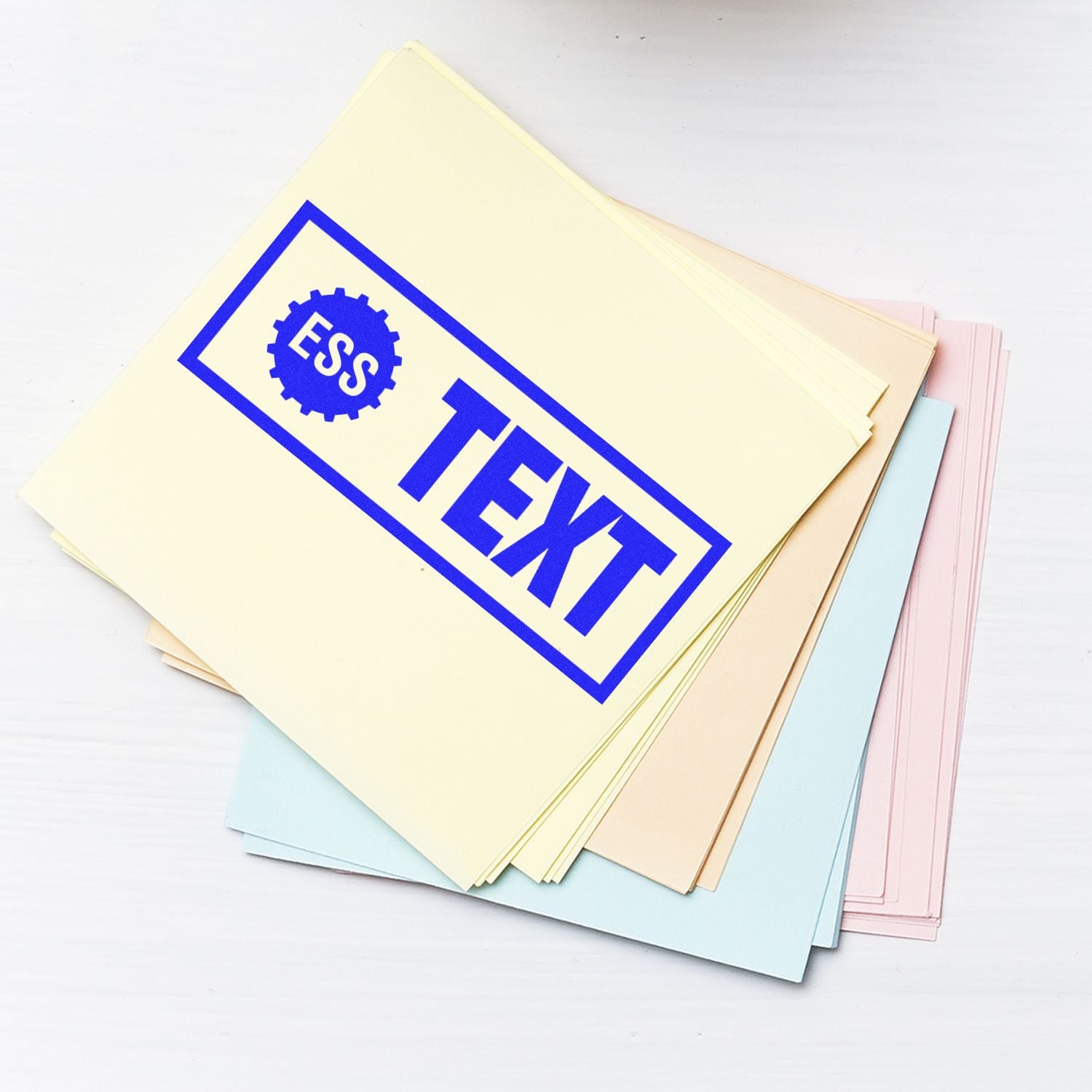 Slim Stamp 1444 Customized Pre-Inked Stamp 1/2 x 1-3/4 used on a stack of pastel-colored papers, displaying ESS TEXT in blue ink.