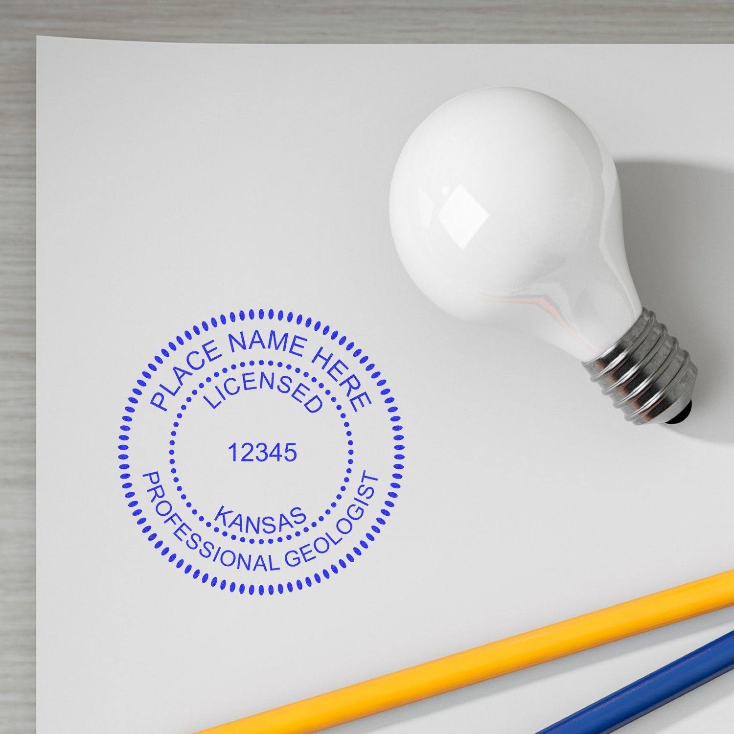 Geologist MaxLight Pre Inked Rubber Stamp of Seal in blue ink on paper beside a light bulb and pencils.