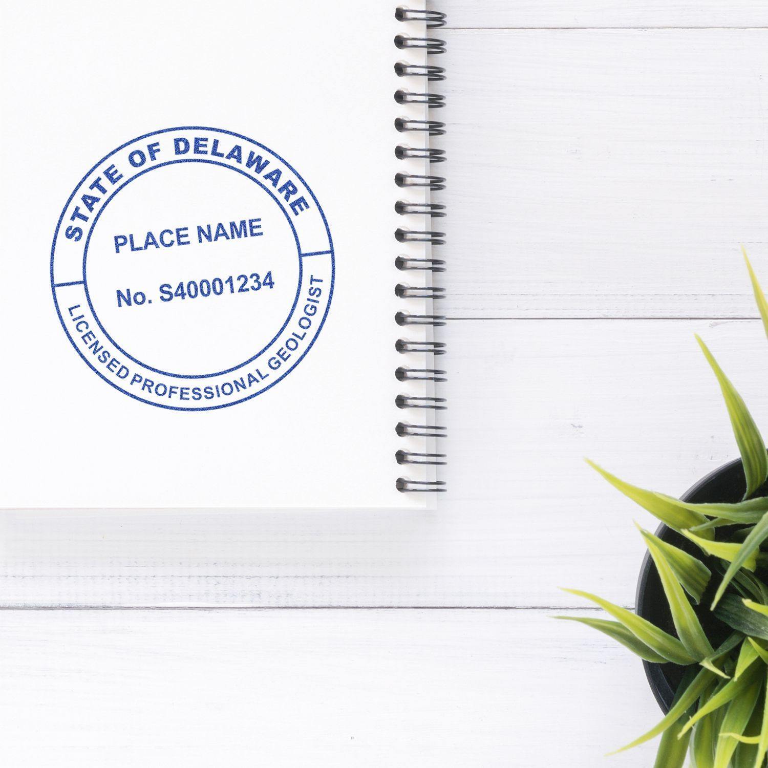 Geologist Slim Pre-Inked Rubber Stamp of Seal on a white notebook with a spiral binding, next to a small green plant on a white desk.