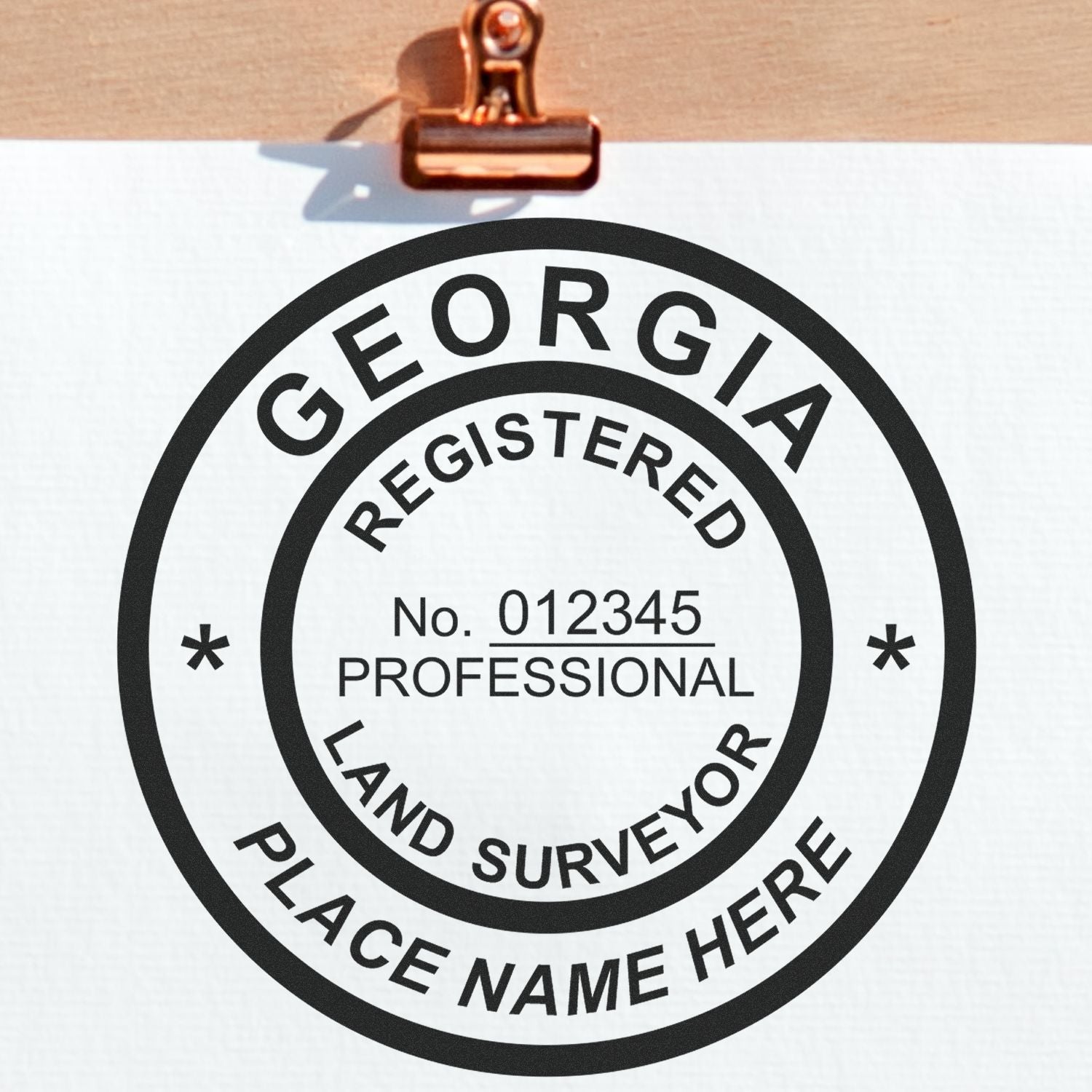Georgia Land Surveyor Seal Stamp, GA PLS Stamp with customizable name and registration number on a white paper clipped to a wooden board.