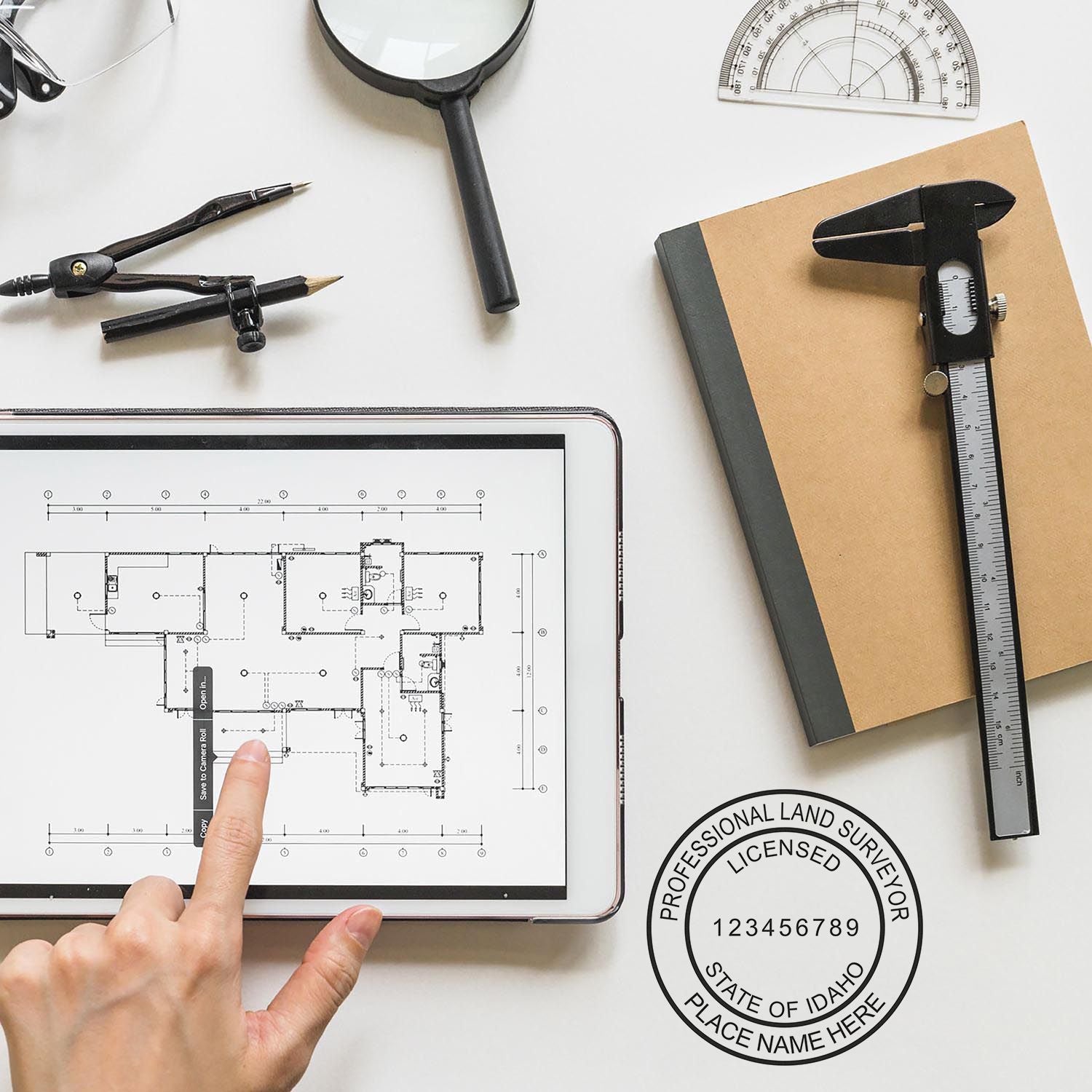 A hand points to a digital blueprint on a tablet, surrounded by surveying tools and a Digital Idaho Land Surveyor Stamp, Electronic Seal for Idaho Land Surveyor.