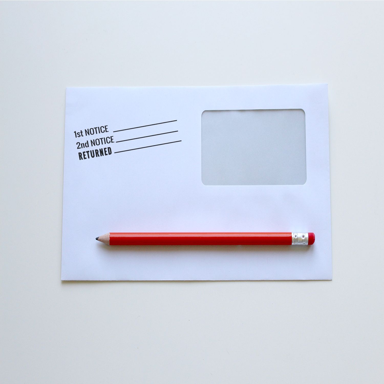 Slim Pre-Inked 1st 2nd Notice Returned Stamp on a white envelope with a red pencil placed diagonally across it.