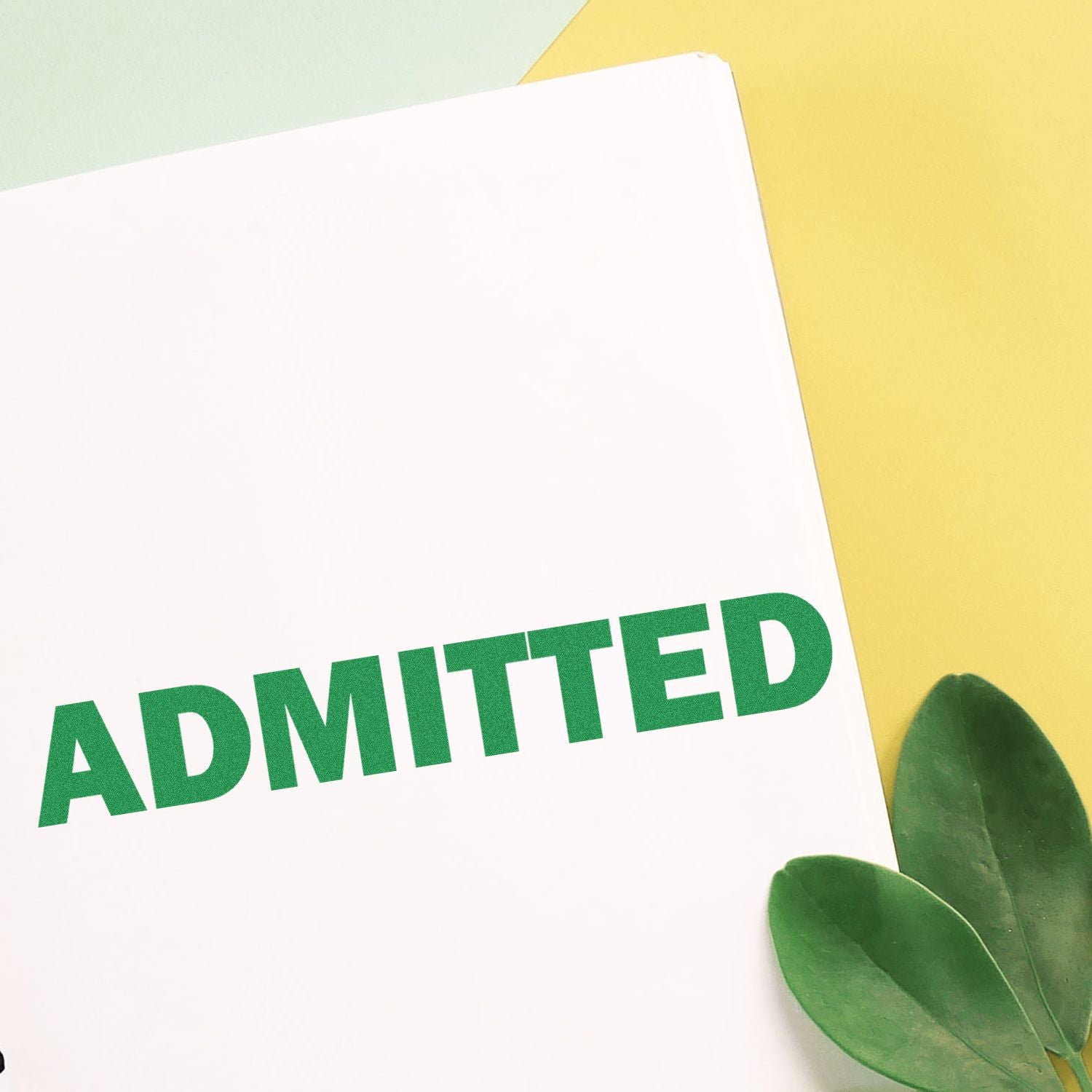 Slim Pre-Inked Admitted Stamp used on a white paper with green 'ADMITTED' text, placed on a yellow and green background.